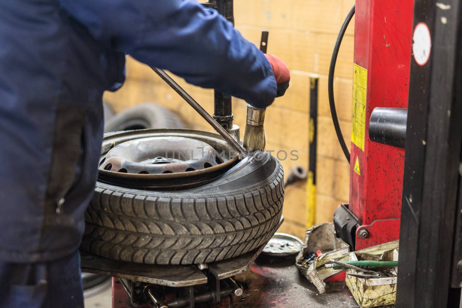 Professional auto mechanic replacing tire on wheel in car repair workshop.