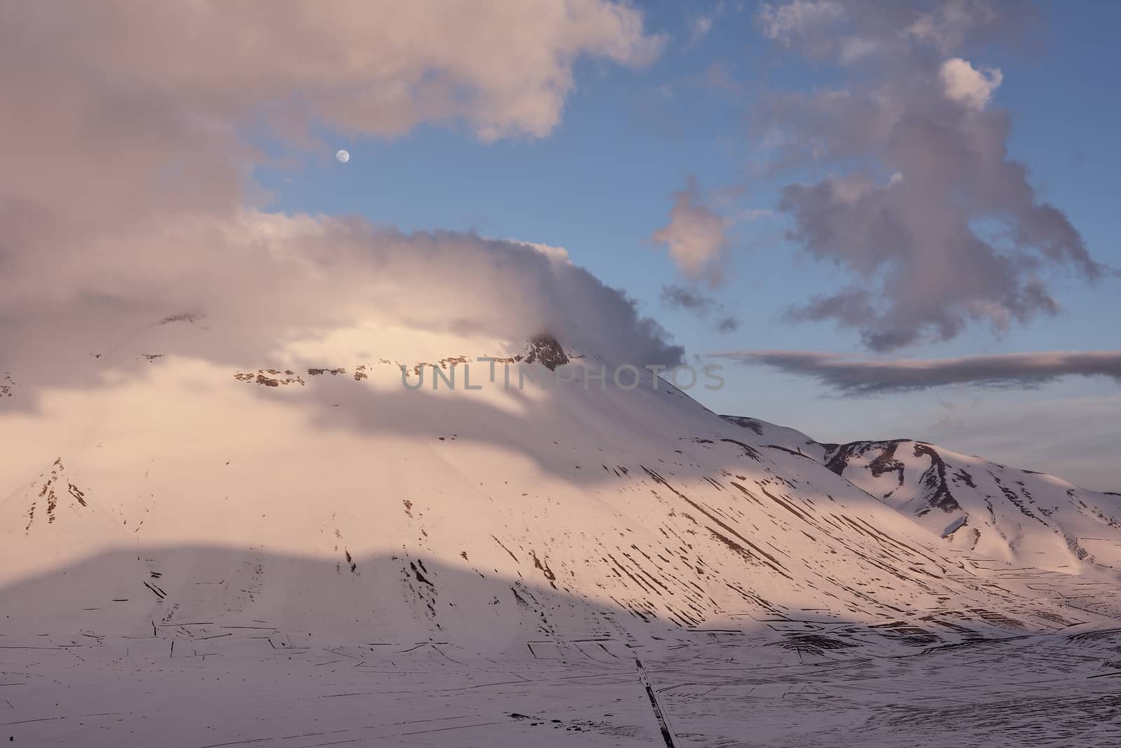 Sunset in the Sibillini mountains and moon in the late winter with snow. Castelluccio, Italy