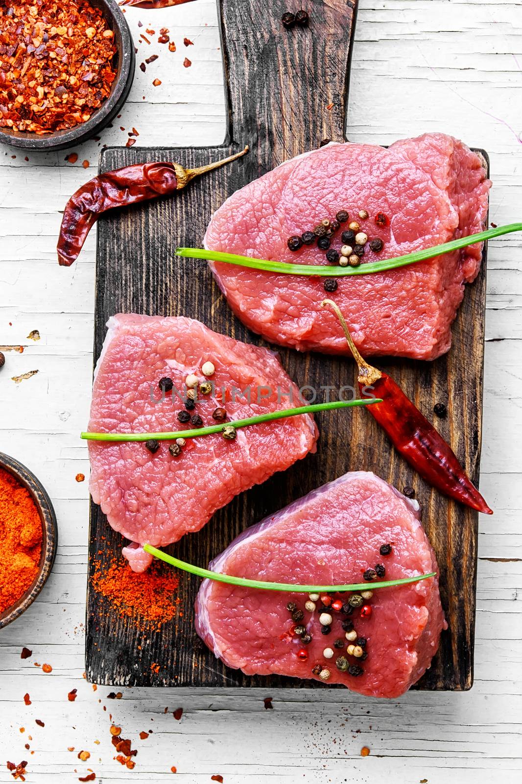 Three raw veal steak with peppers and spices