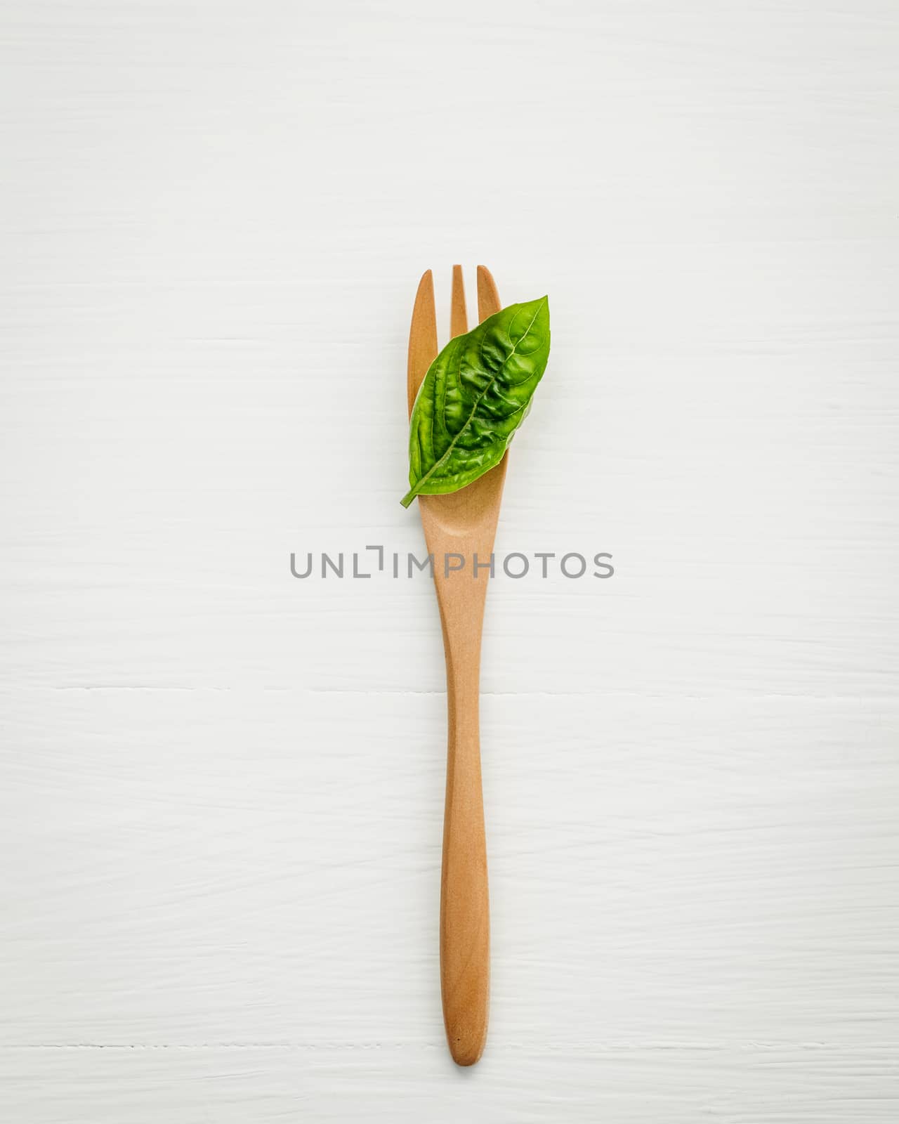 Closeup  fresh sweet basil leaves with fork  on white wooden background. Sweet basil leaves with flat lay .
