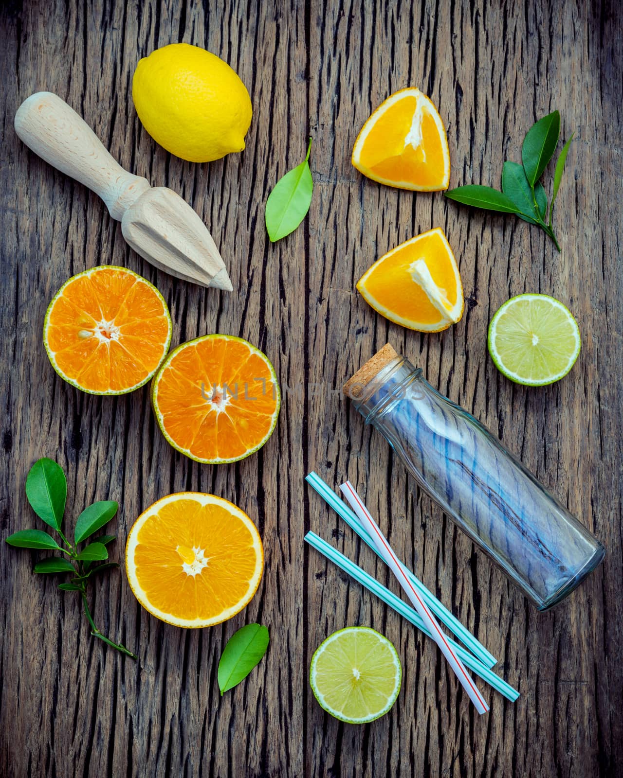 Mixed fresh citrus fruits and orange leaves background. Ingredients for summer citrus juice with juicer and glass bottle .Fresh lemons, lime and oranges set up on shabby wooden table with flat lay.