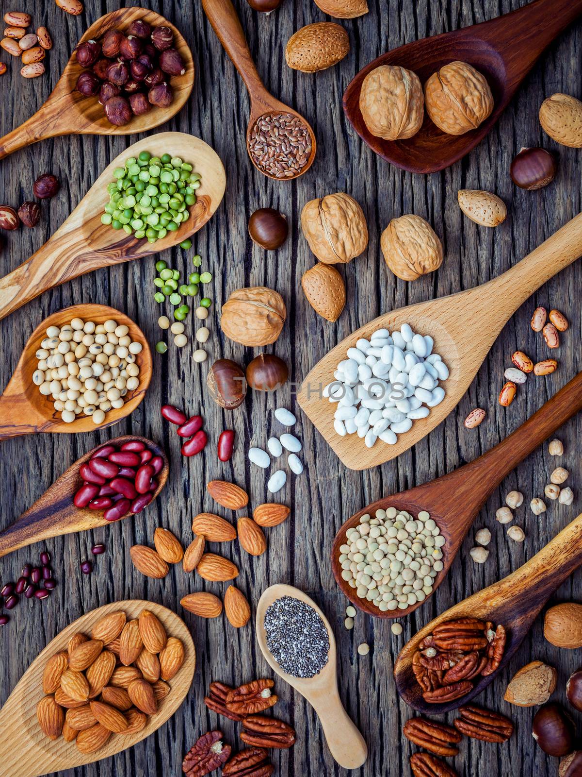Various legumes and different kinds of nutshells in spoons. Walnuts kernels ,hazelnuts, almond ,brown pinto ,soy beans ,flax seeds ,chia ,chickpea ,red kidney beans and pecan on shabby wooden table.