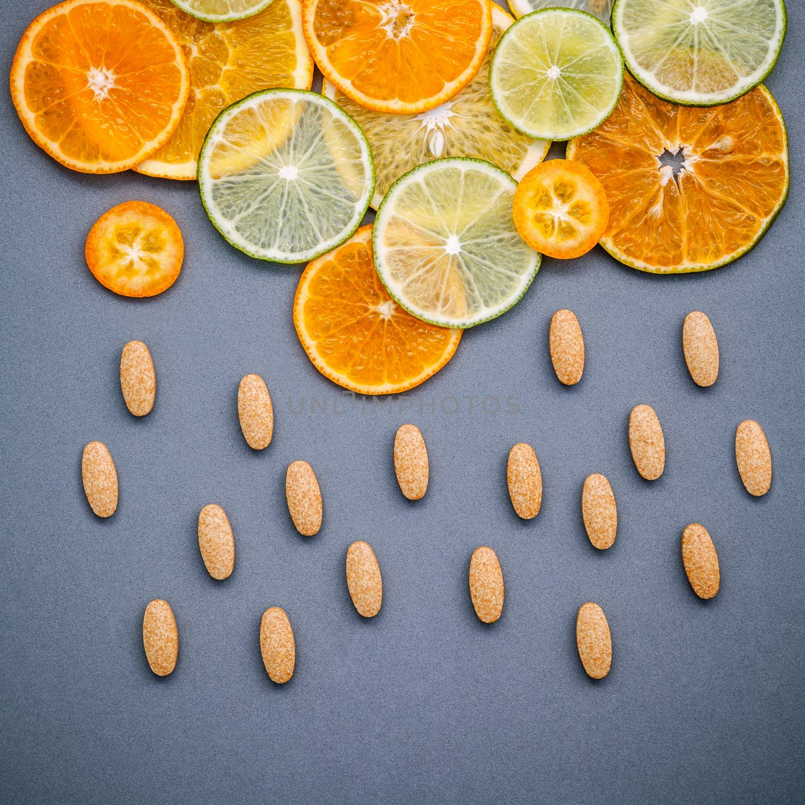Healthy foods and medicine concept. Pills of vitamin C and various citrus fruits sliced in the shape of cloud and raining. Mixed citrus fruits sliced lime,orange and lemon on gray background flat lay.