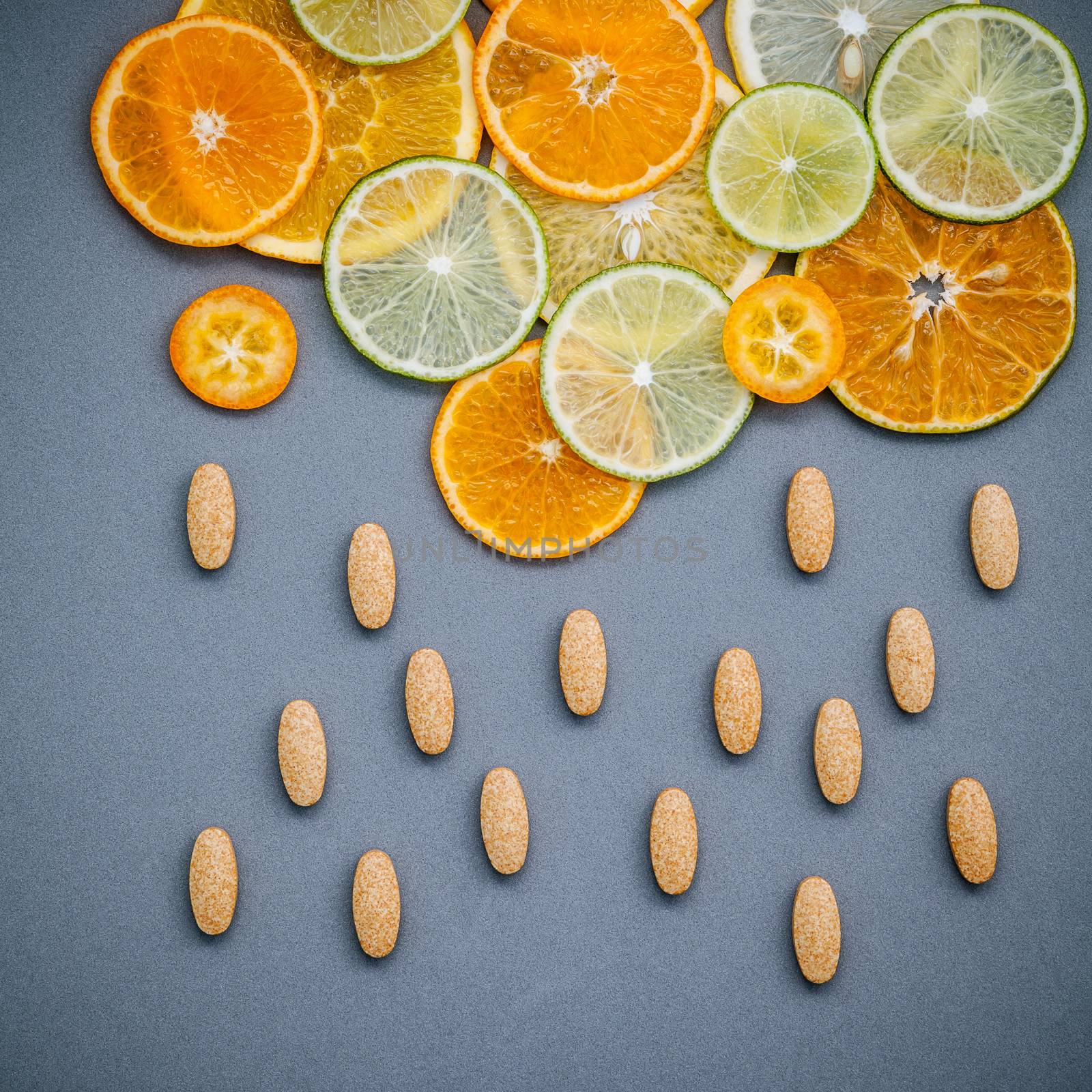 Healthy foods and medicine concept. Pills of vitamin C and citrus fruits in the shape of cloud and raining. Citrus fruits sliced lime,orange and lemon on gray background flat lay.