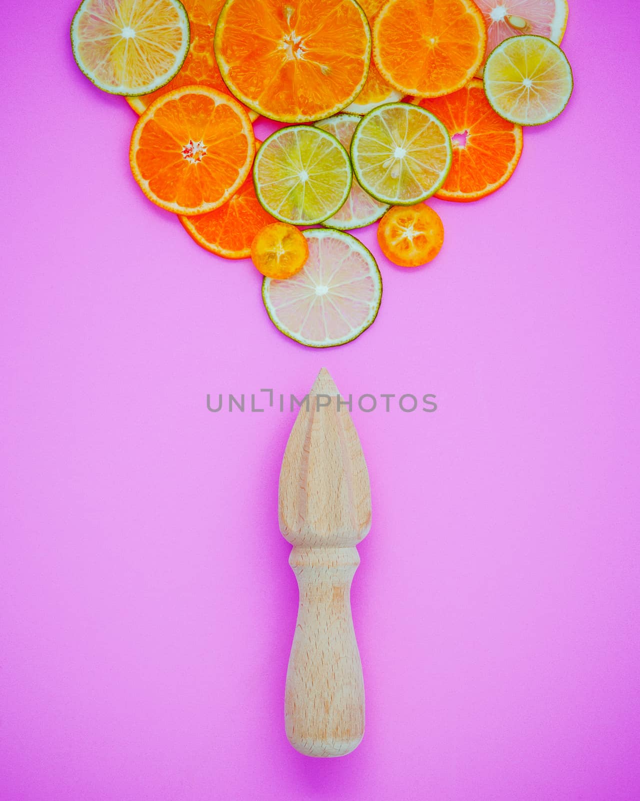 Mixed fresh citrus fruits and wooden juicer for summer citrus juice. Citrus fruits sliced lime,orange and lemon on light pink background flat lay.
