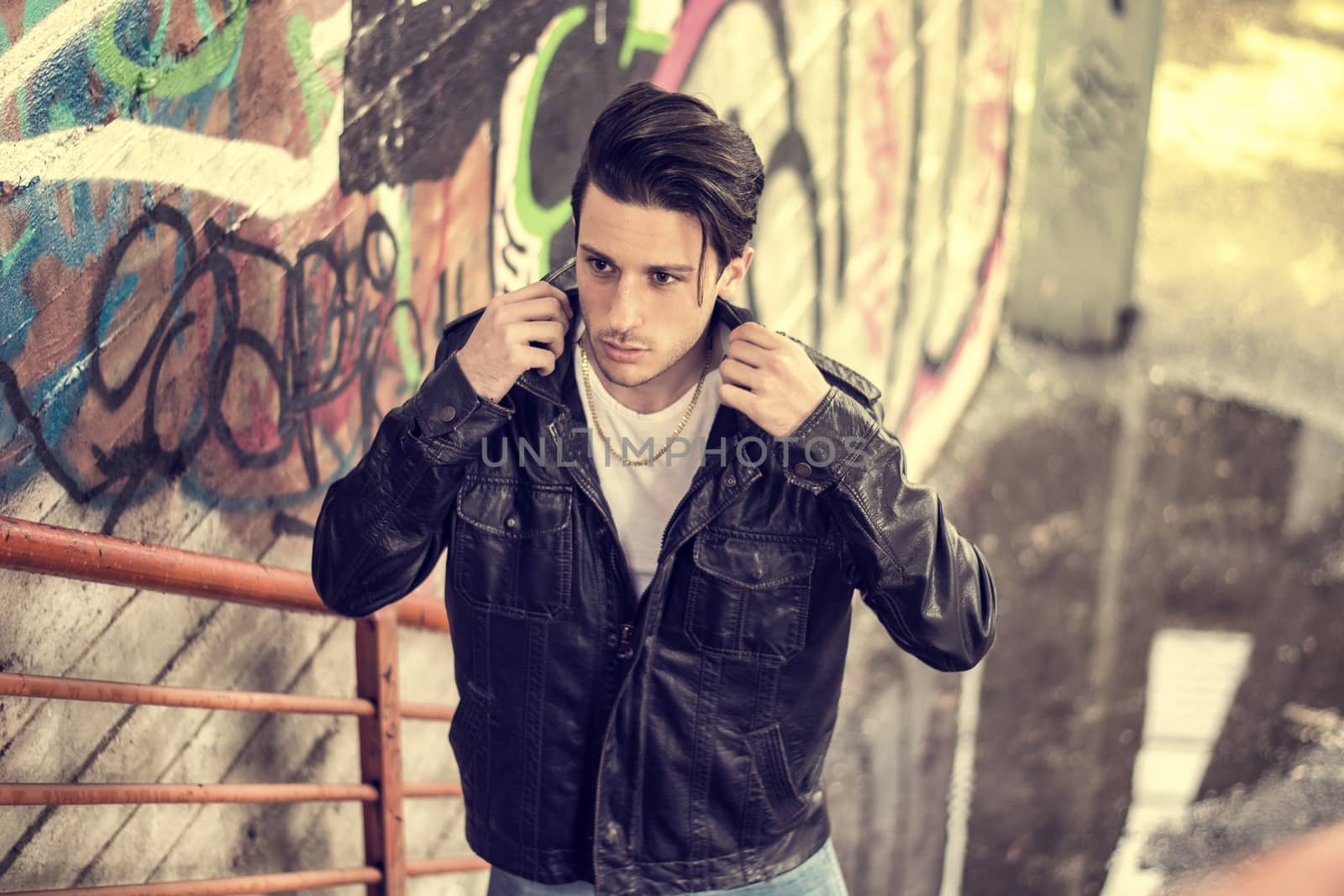 Handsome young man standing outdoors in urban environment on metal stairs, looking at camera