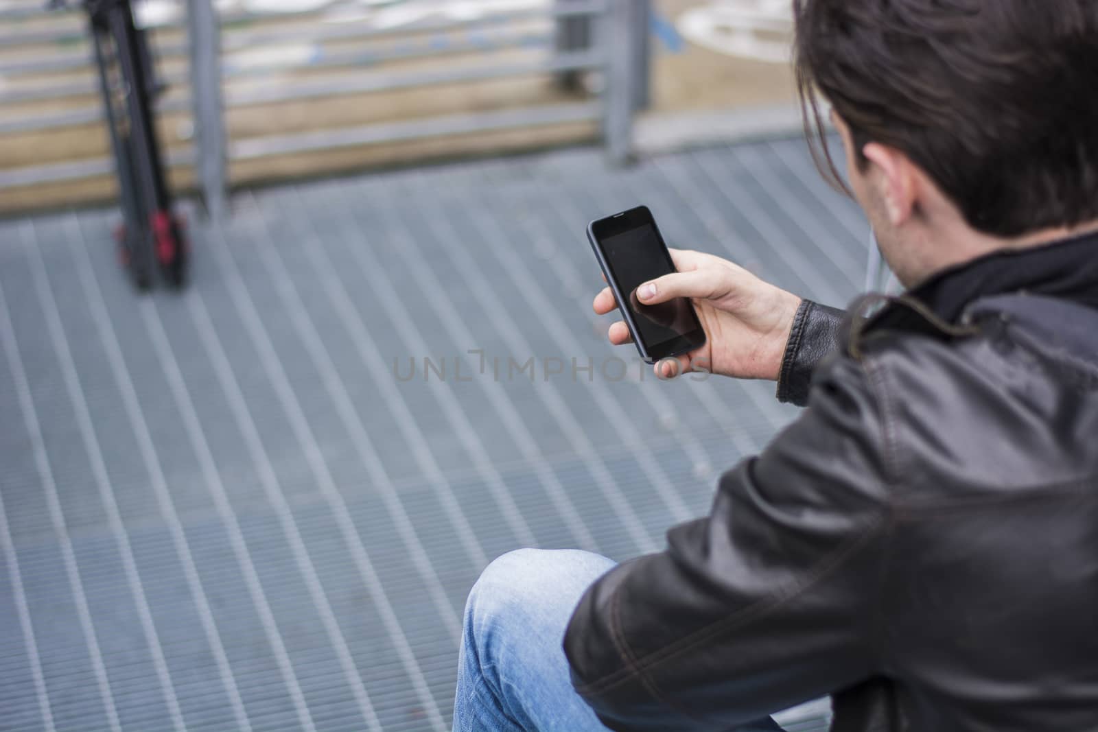 Handsome young man standing outdoors in urban environment on metal stairs, using cell phone