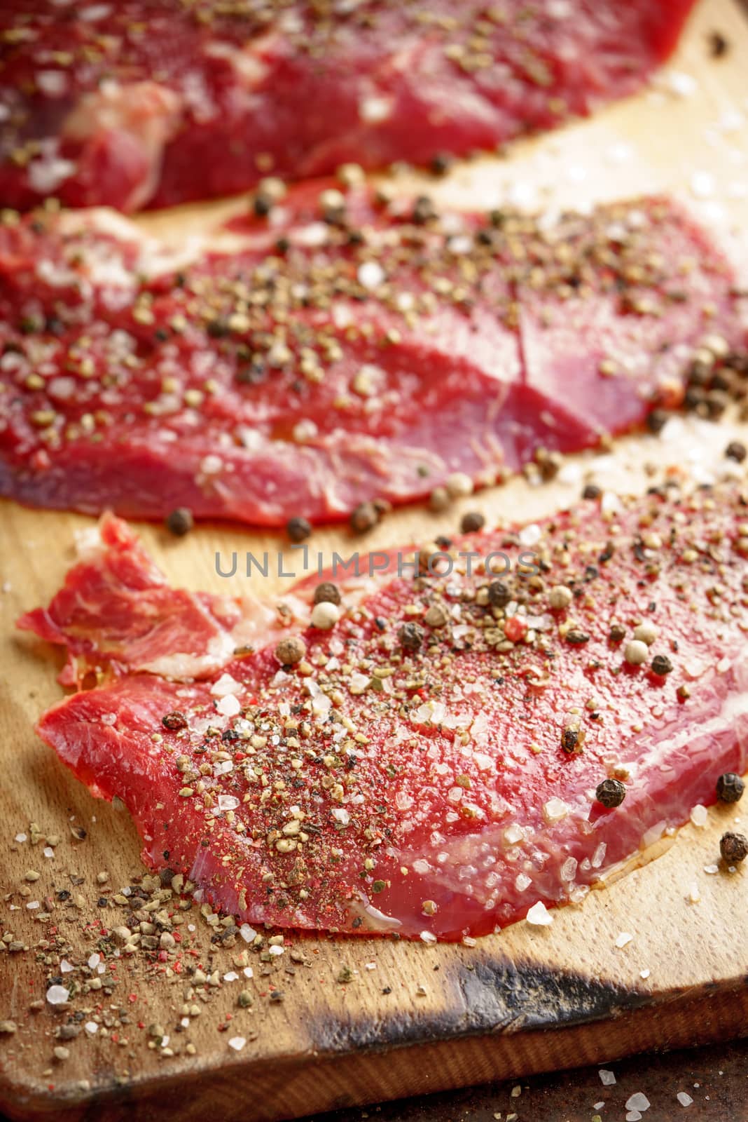 Raw beef steak and spicel on cutting board on the table by Deniskarpenkov