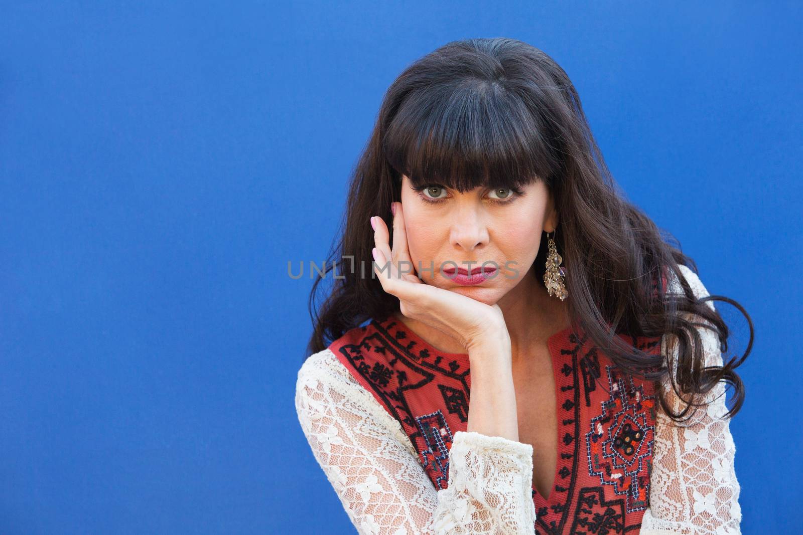 Gorgeous woman sitting front of blank blue wall with chin resting on hand