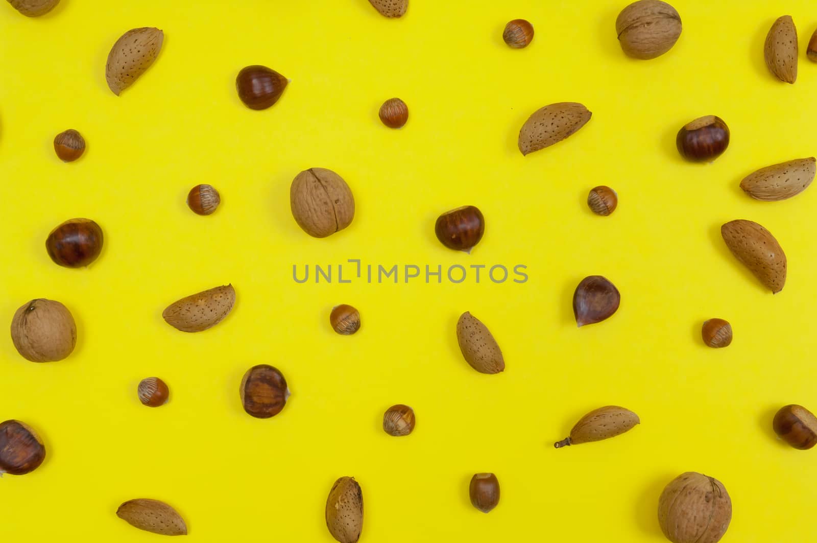 Setting of in shell almonds, chestnuts and hazelnuts on yellow background top view