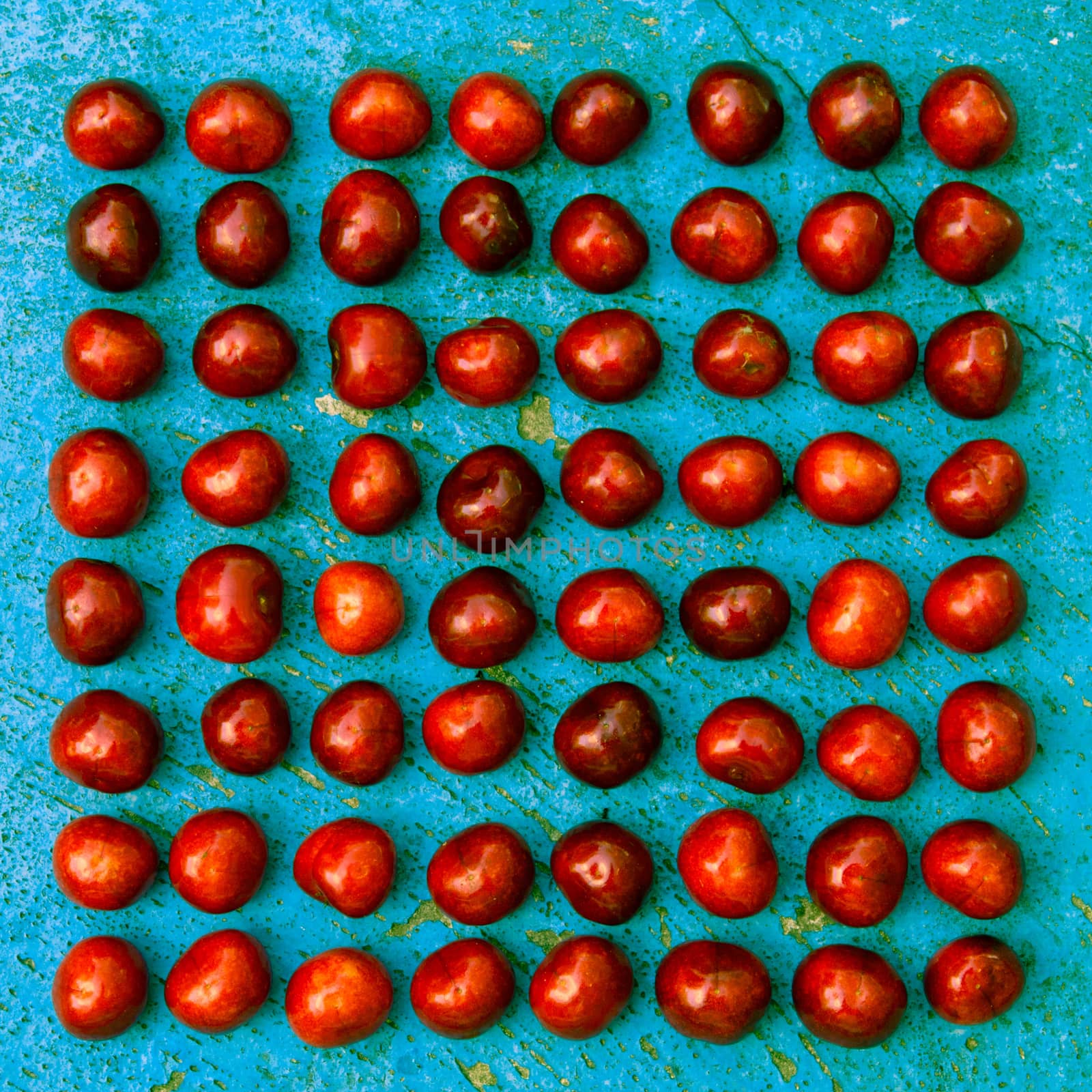 Square arrangement of ripe cherries on blue textrured background, cherry pattern