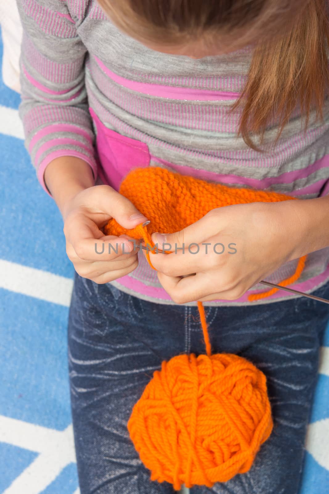 Top view of the child who knits with needles scarf orange thread by Madhourse
