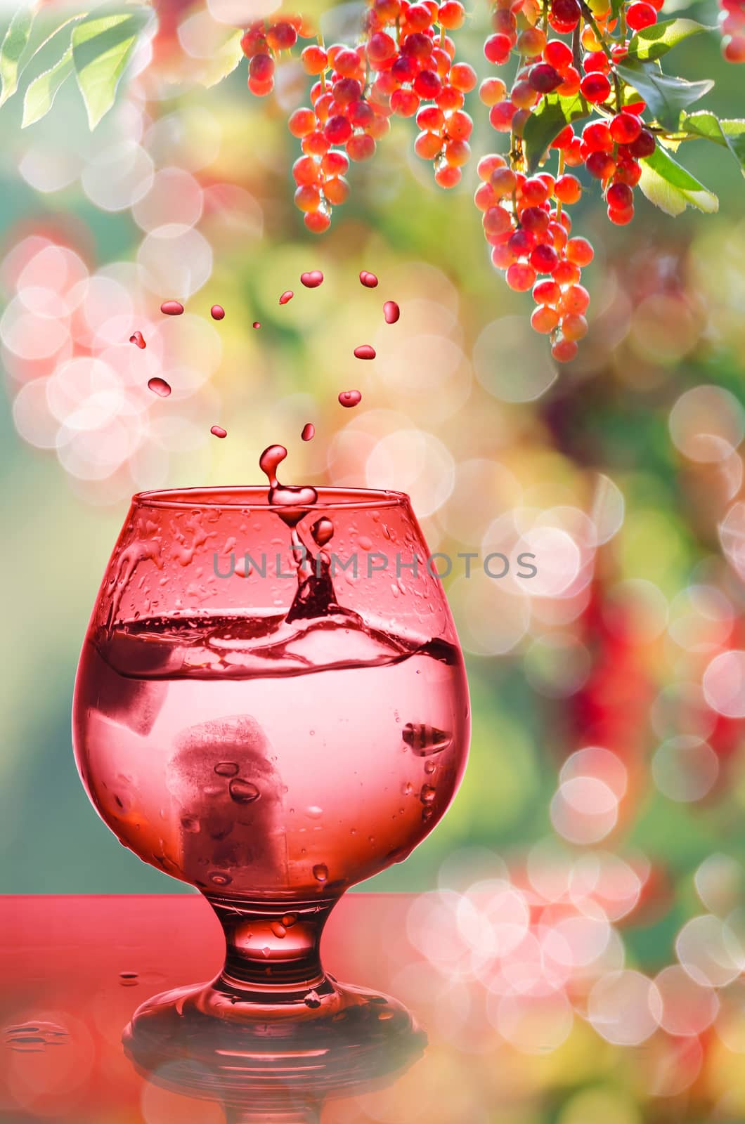 Cocktail glass with ice and drops in the heart, painted red. Background with natural bokeh with sunlight and berries.