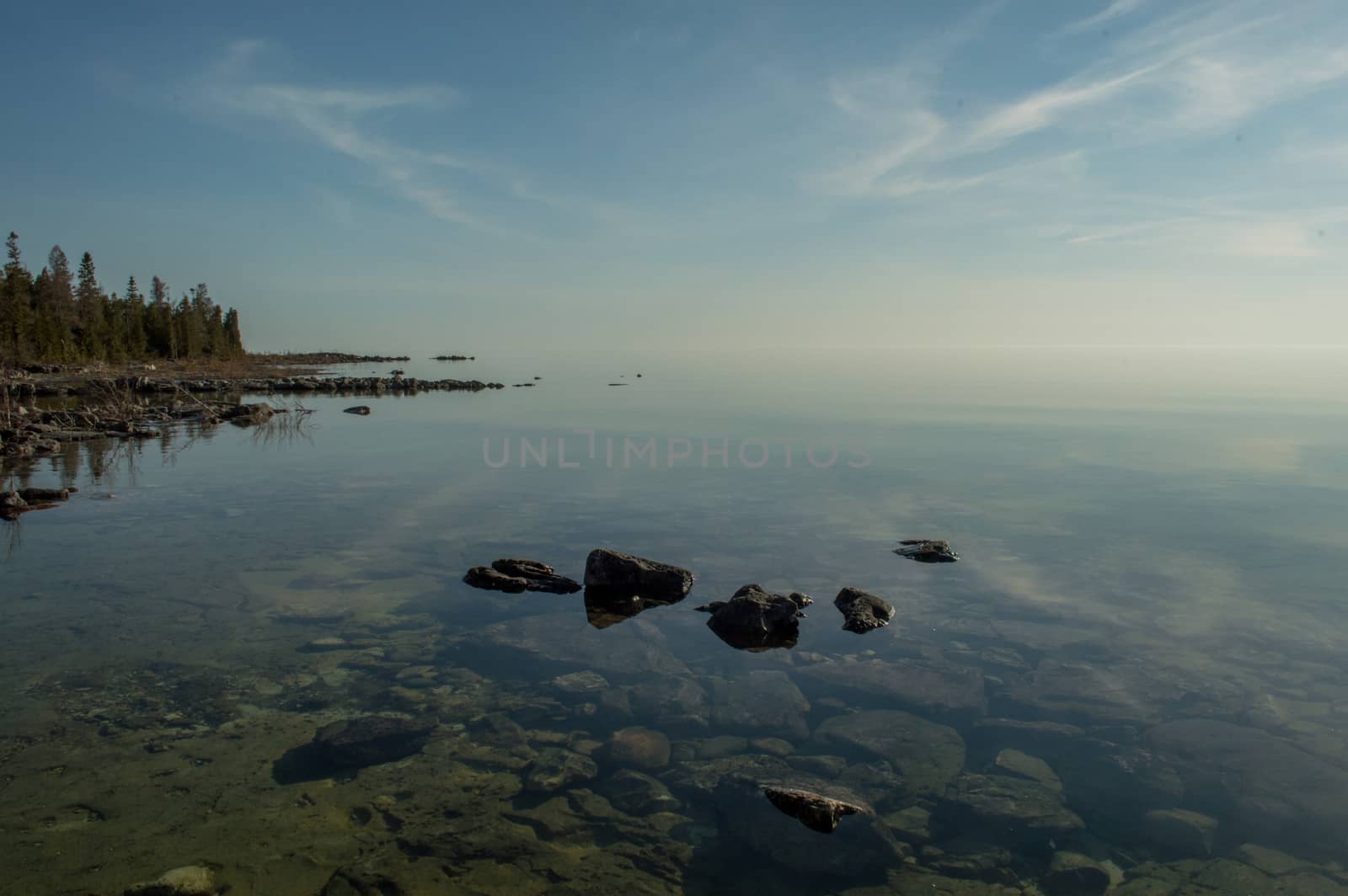 Dead calm afternoon image of clear lake huron water and limestone rocks along shoreline.  Clouds reflecting in a zign zag.