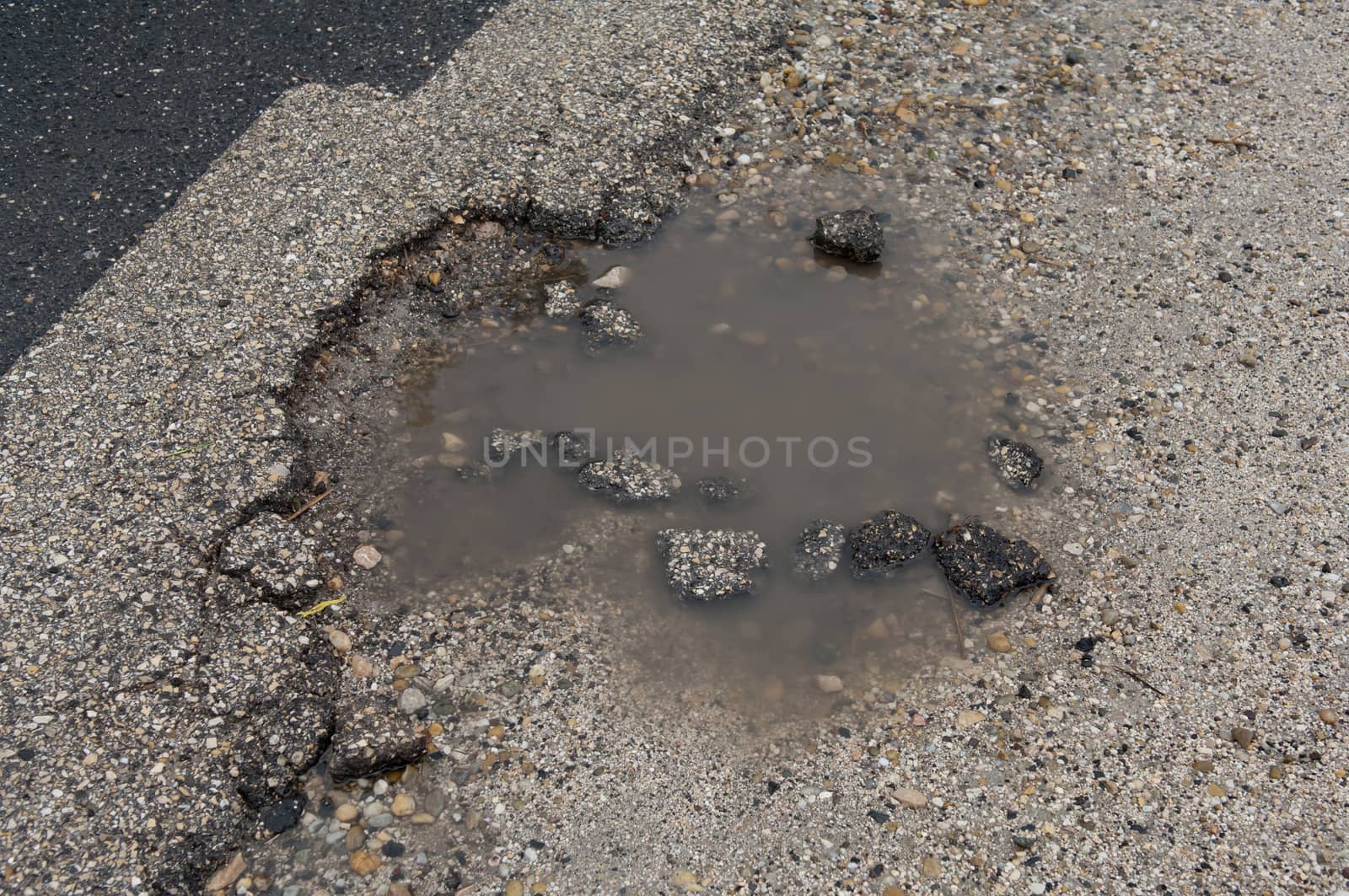 Asphalt road with pothole filled with water and asphalt pieces