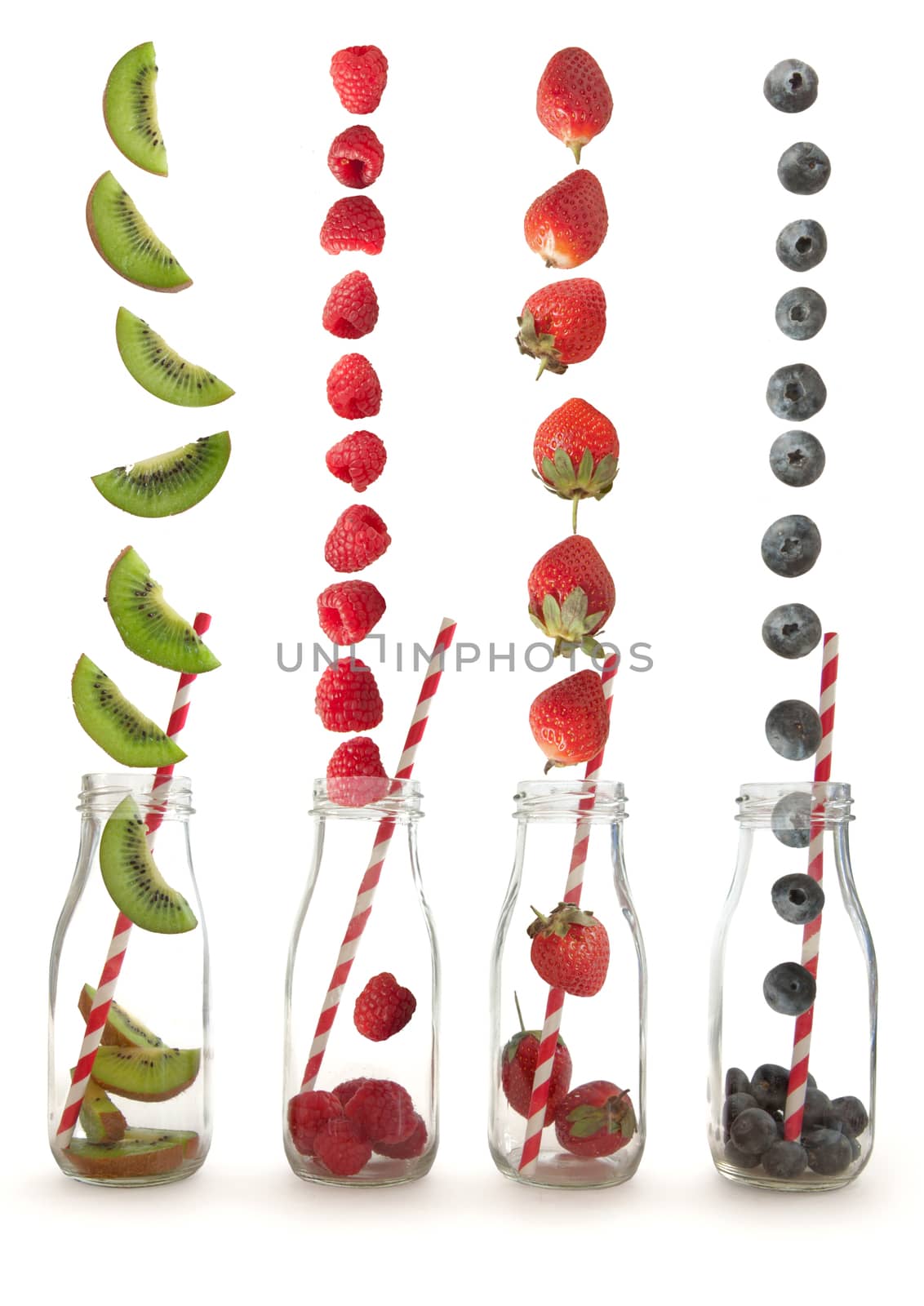Berry fruits and kiwi falling into glass bottles with straws over a white background
