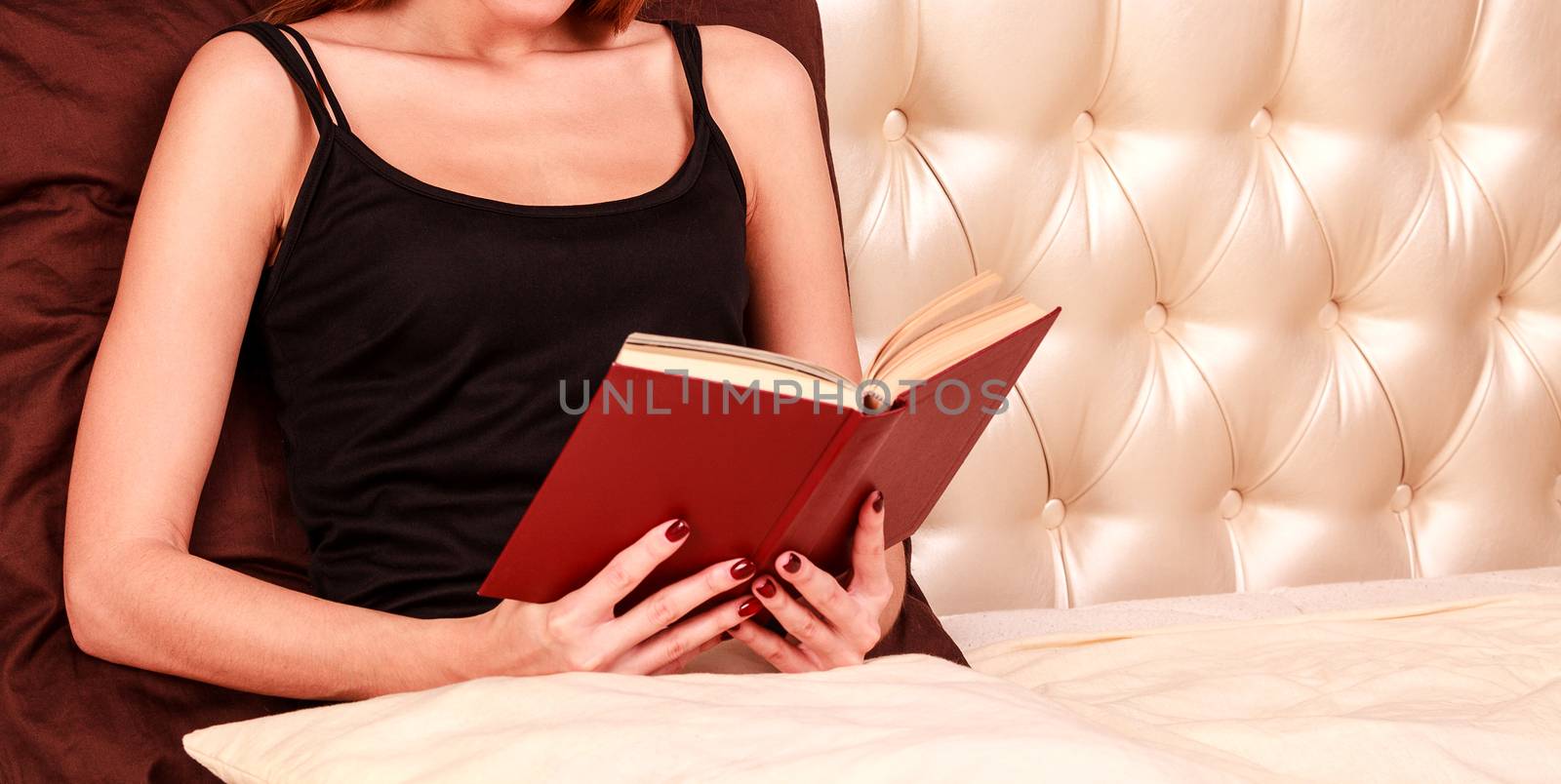 close up of young woman reading book in bed