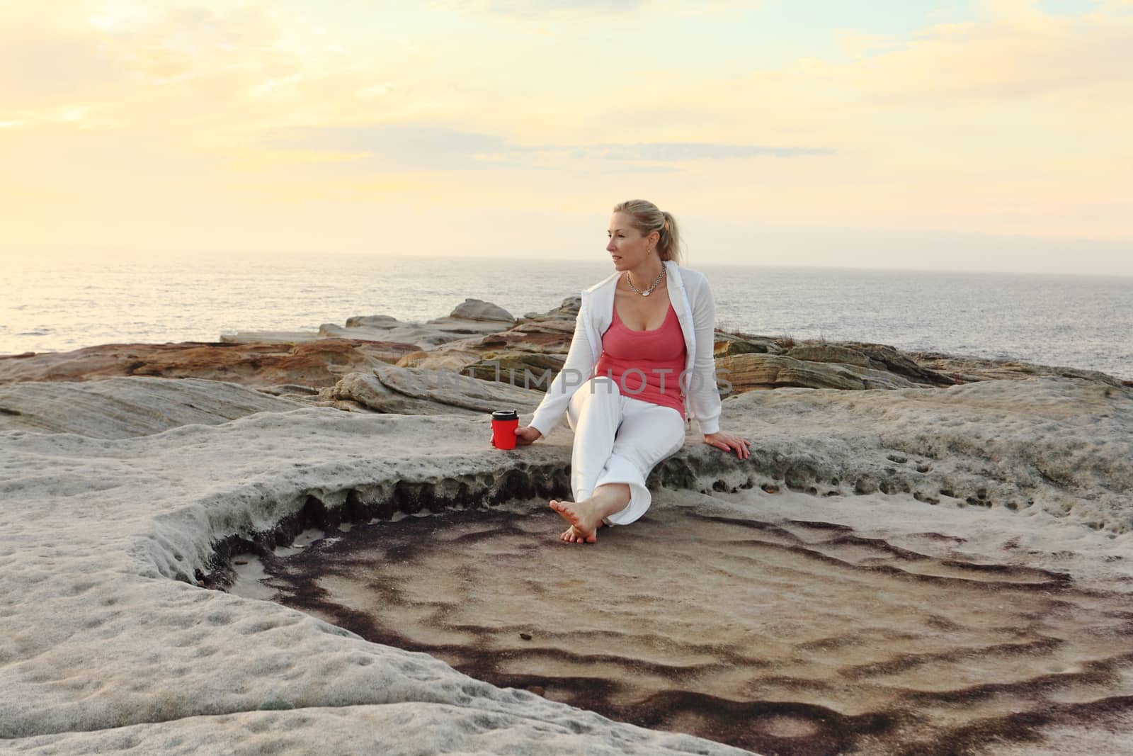 A woman relaxes by the ocean enjoying her morning coffee