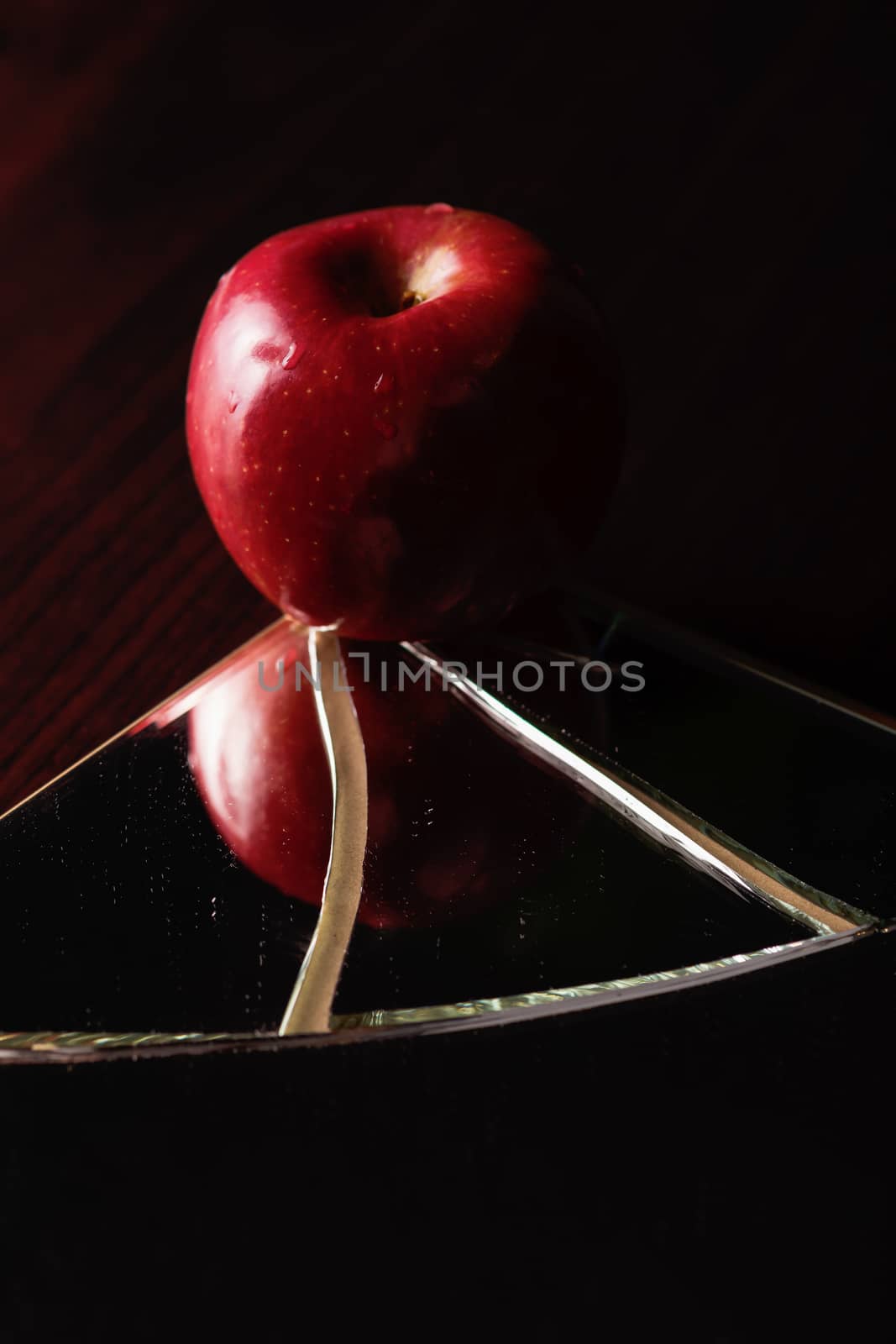 Red apple on cracked broken mirror reflecting