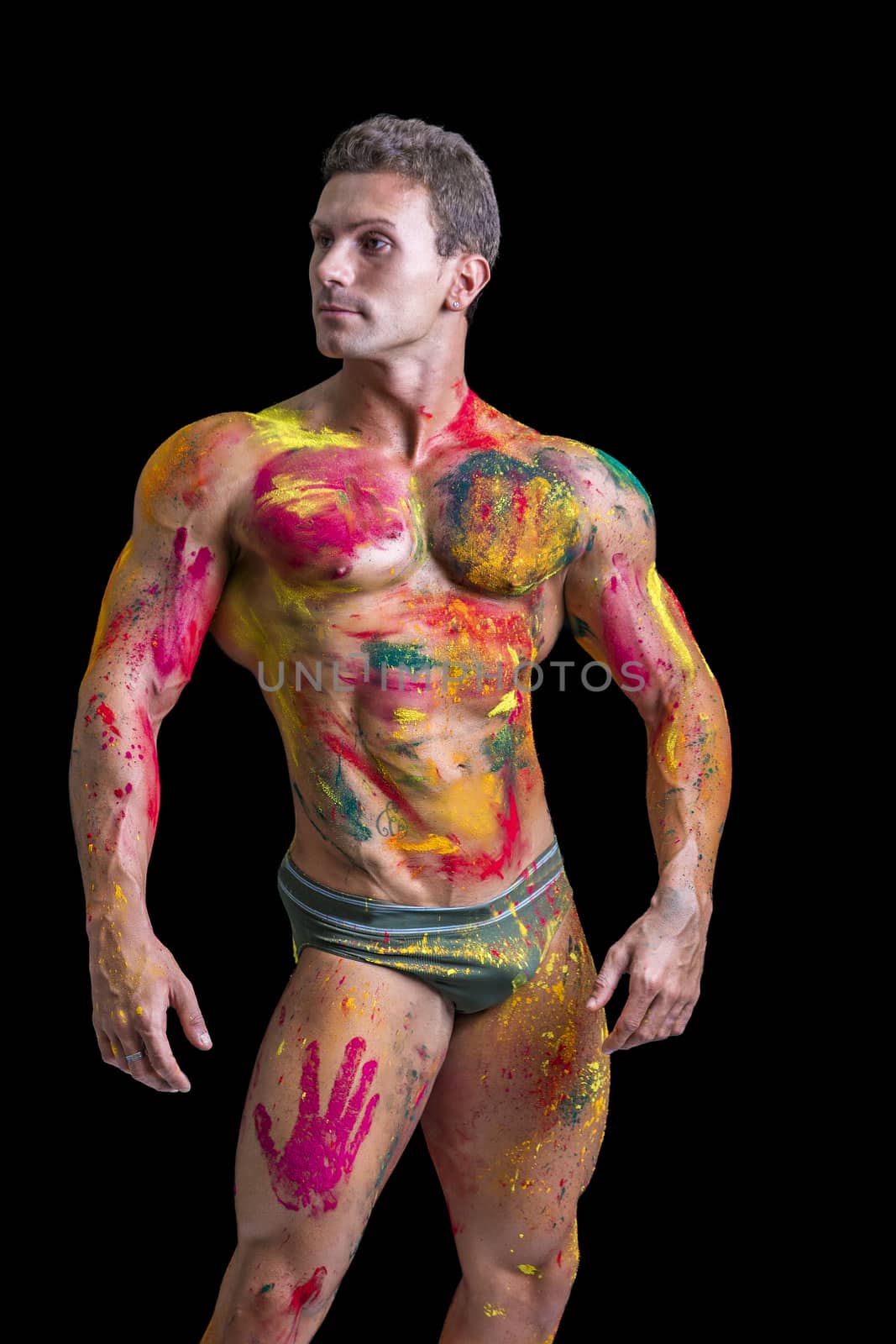 Muscular young man shirtless with skin painted with Holi colors, looking down, isolated on white
