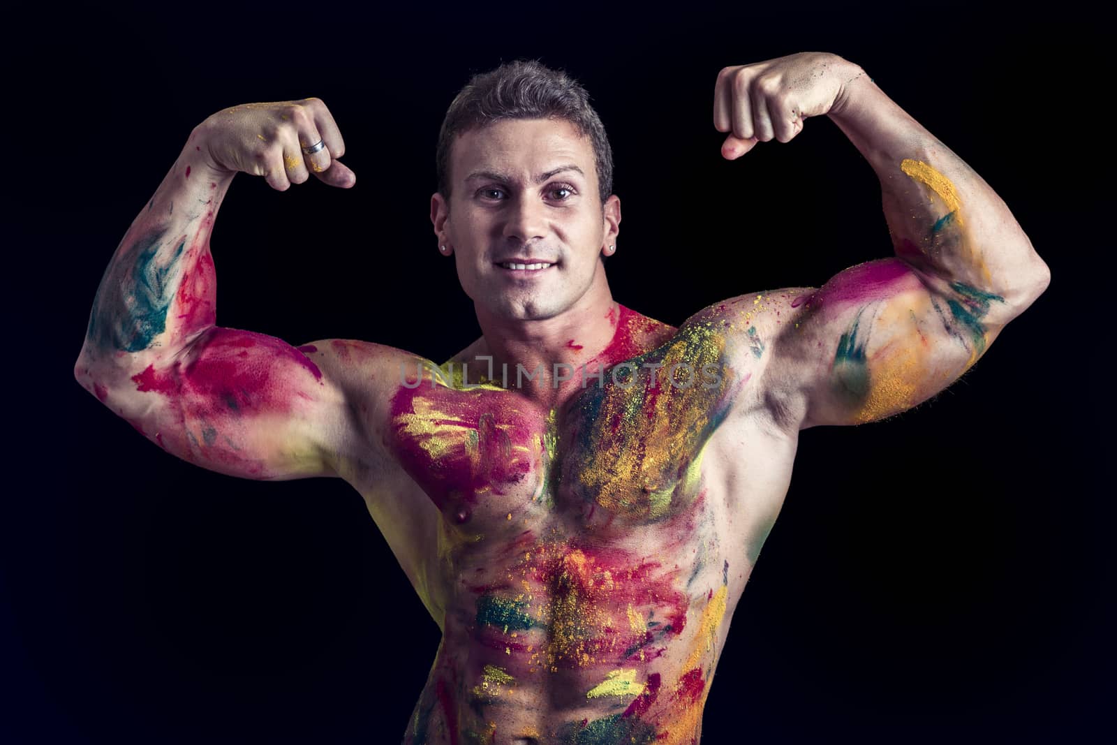 Muscular young man shirtless with skin painted with Holi colors, looking down, isolated on white