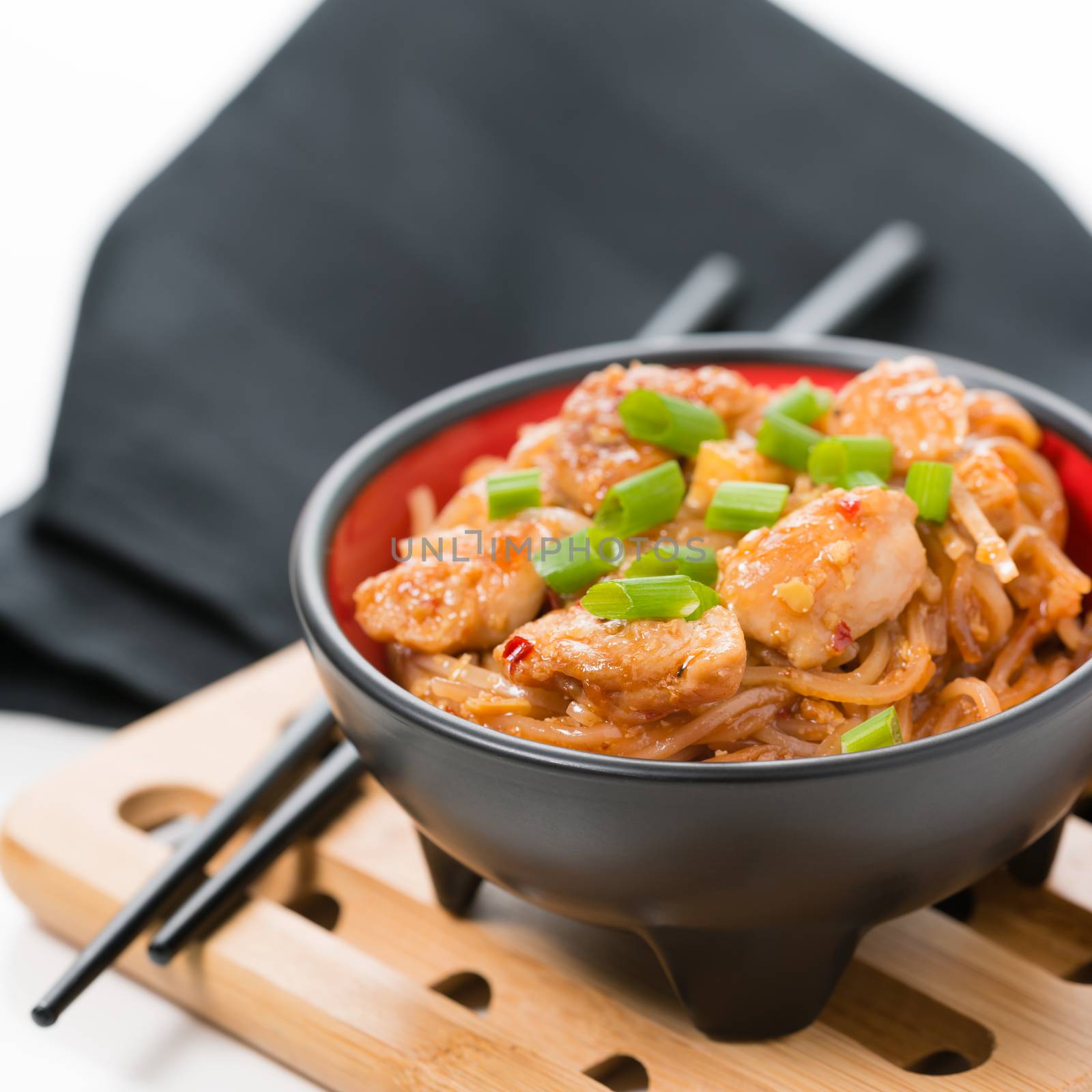 Closeup view of spicy chicken pad thai on a bamboo trivet.