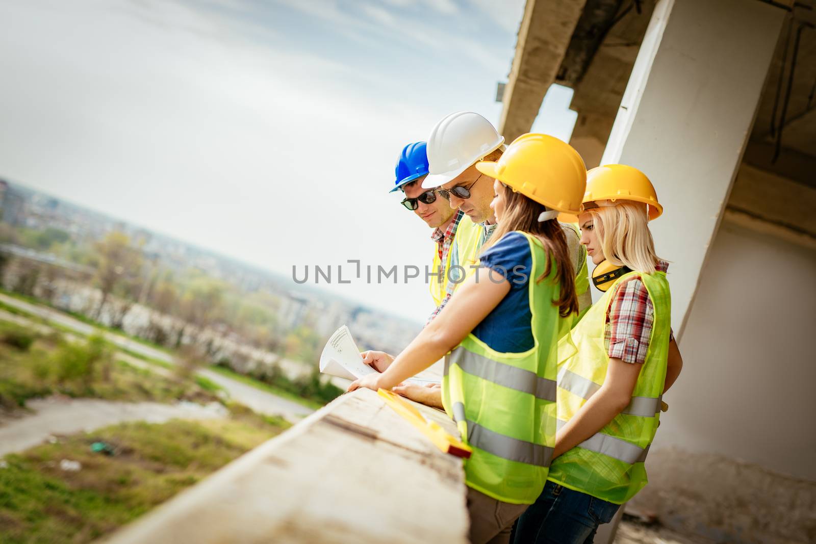 Four construction architects review plan at a construction site.