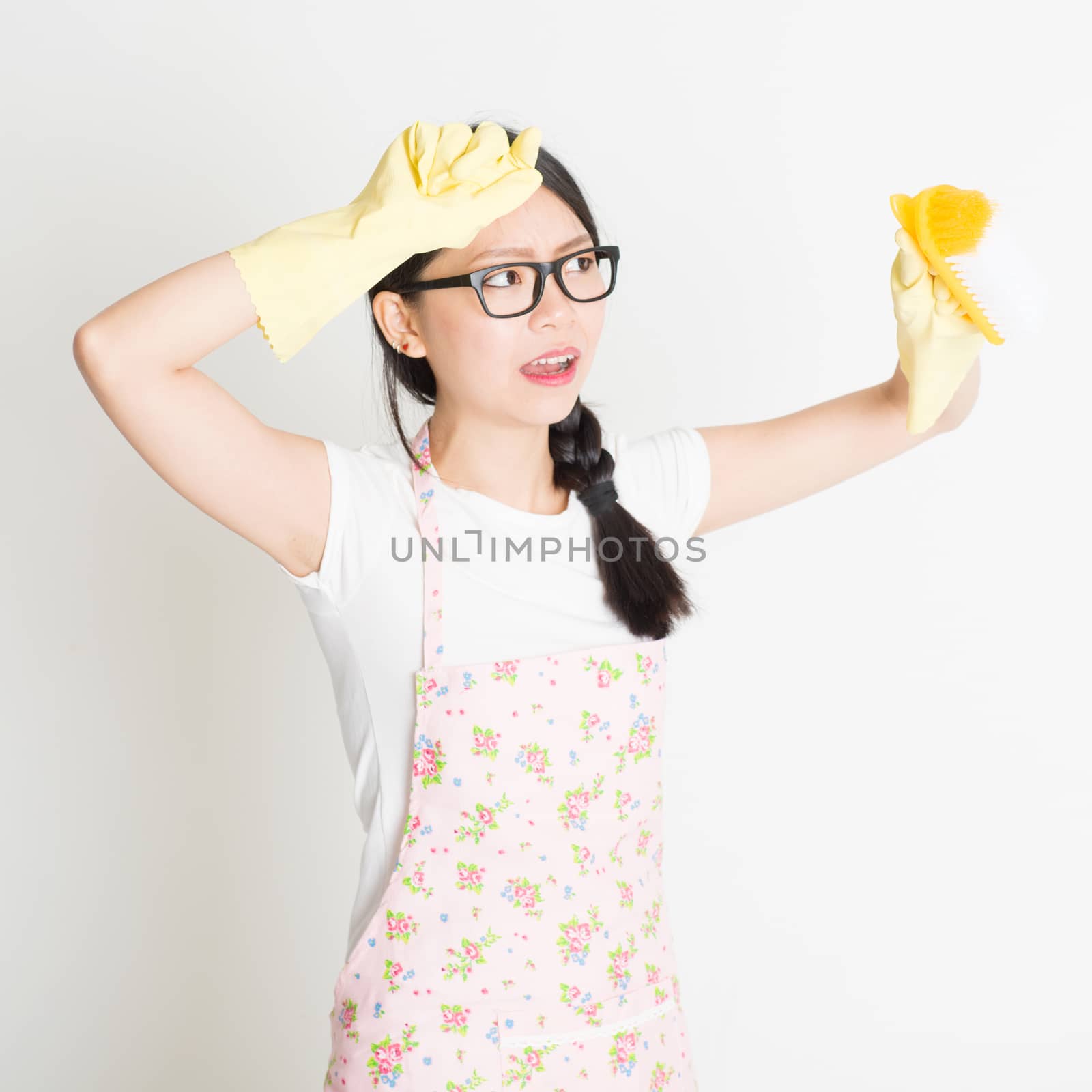Young Asian woman with rubber gloves cleaning house with brush.