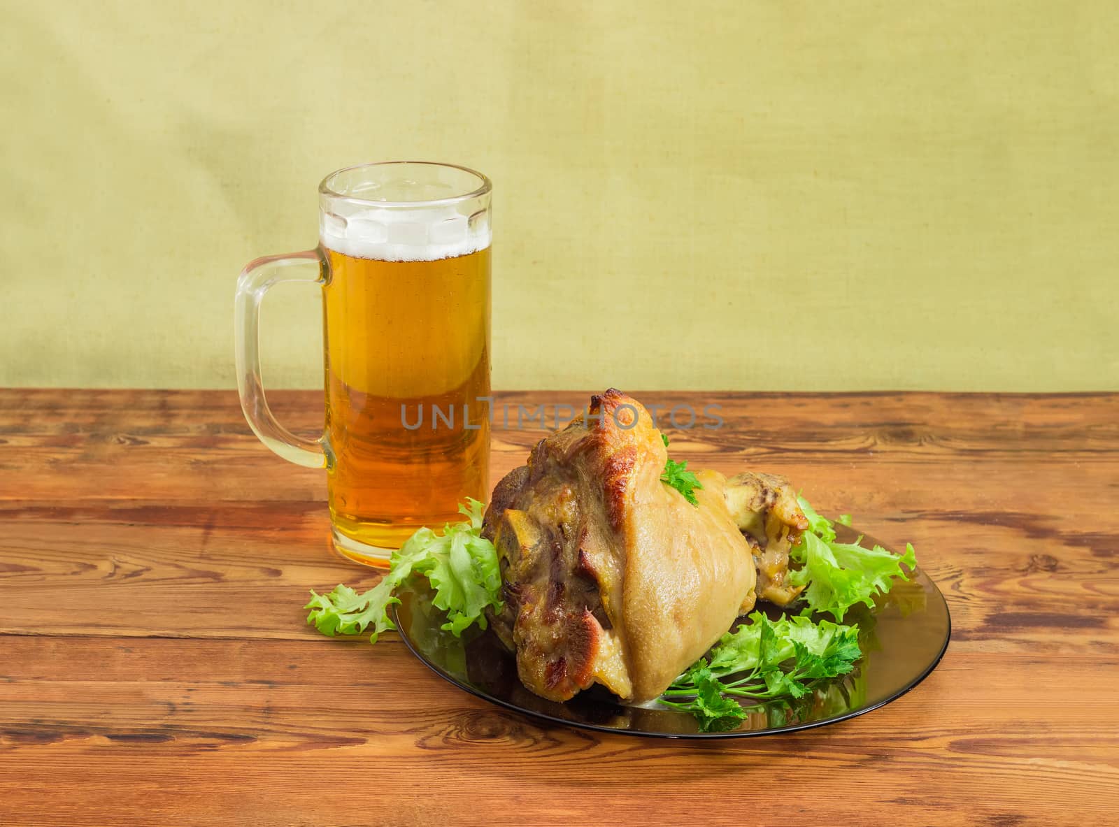 Baked ham hock with lettuce and parsley on a glass dish and glass of lager beer on an old wooden surface
