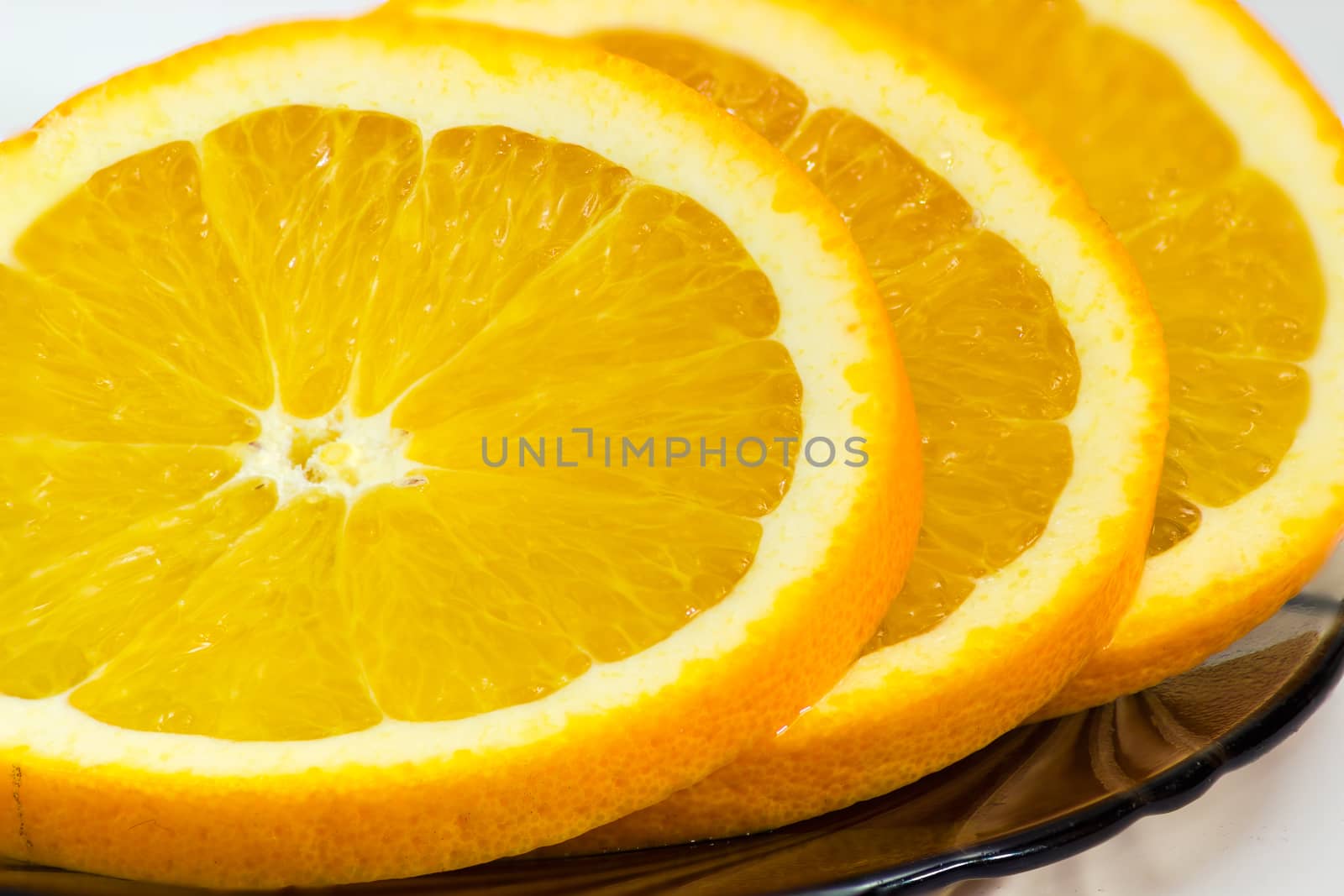 Fragment of several slices of an fresh orange closeup on a glass saucer on a light background
