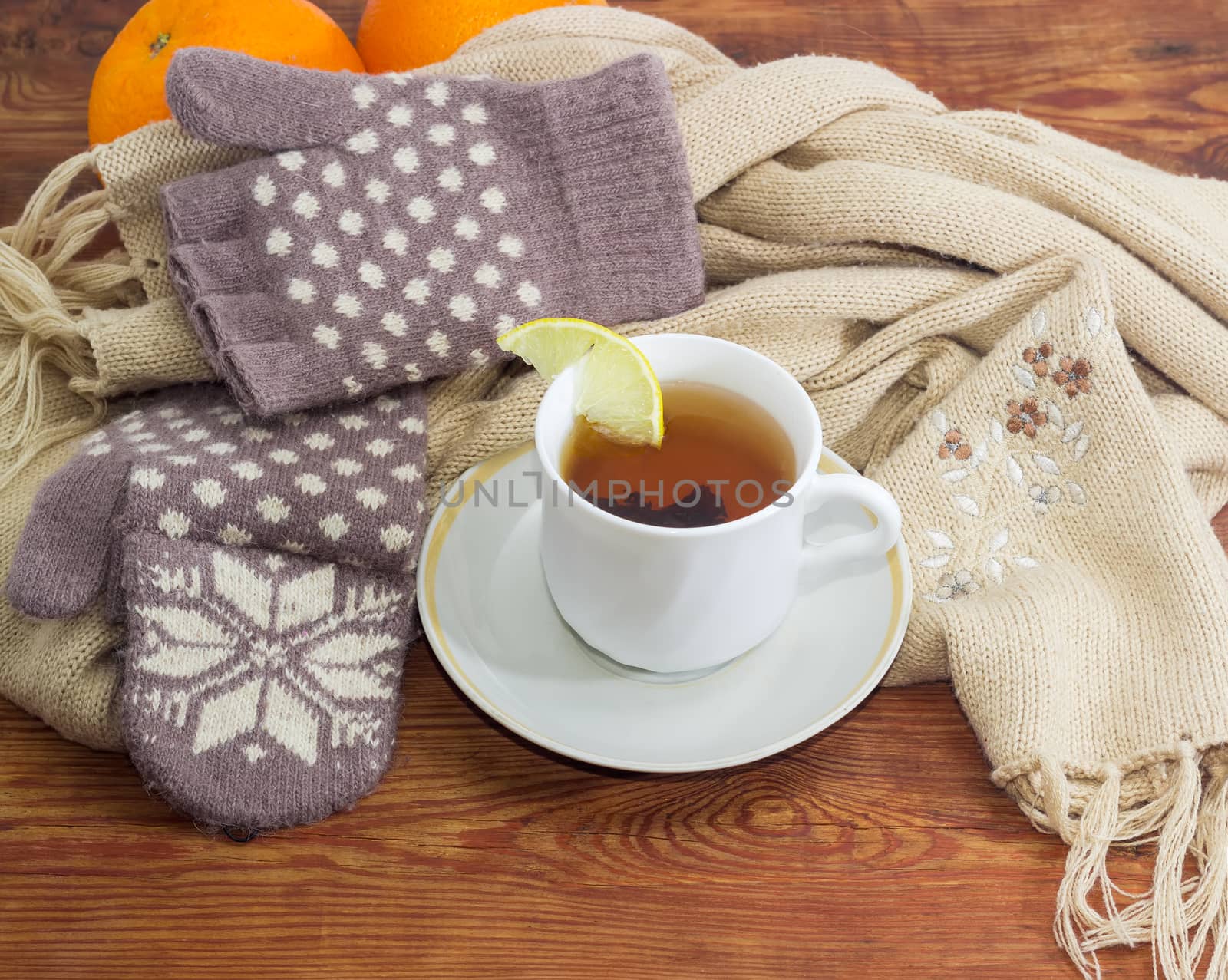 Cup of black tea with lemon on a background of women's woolen hybrid mittens and thick knitted scarf on wooden surface
