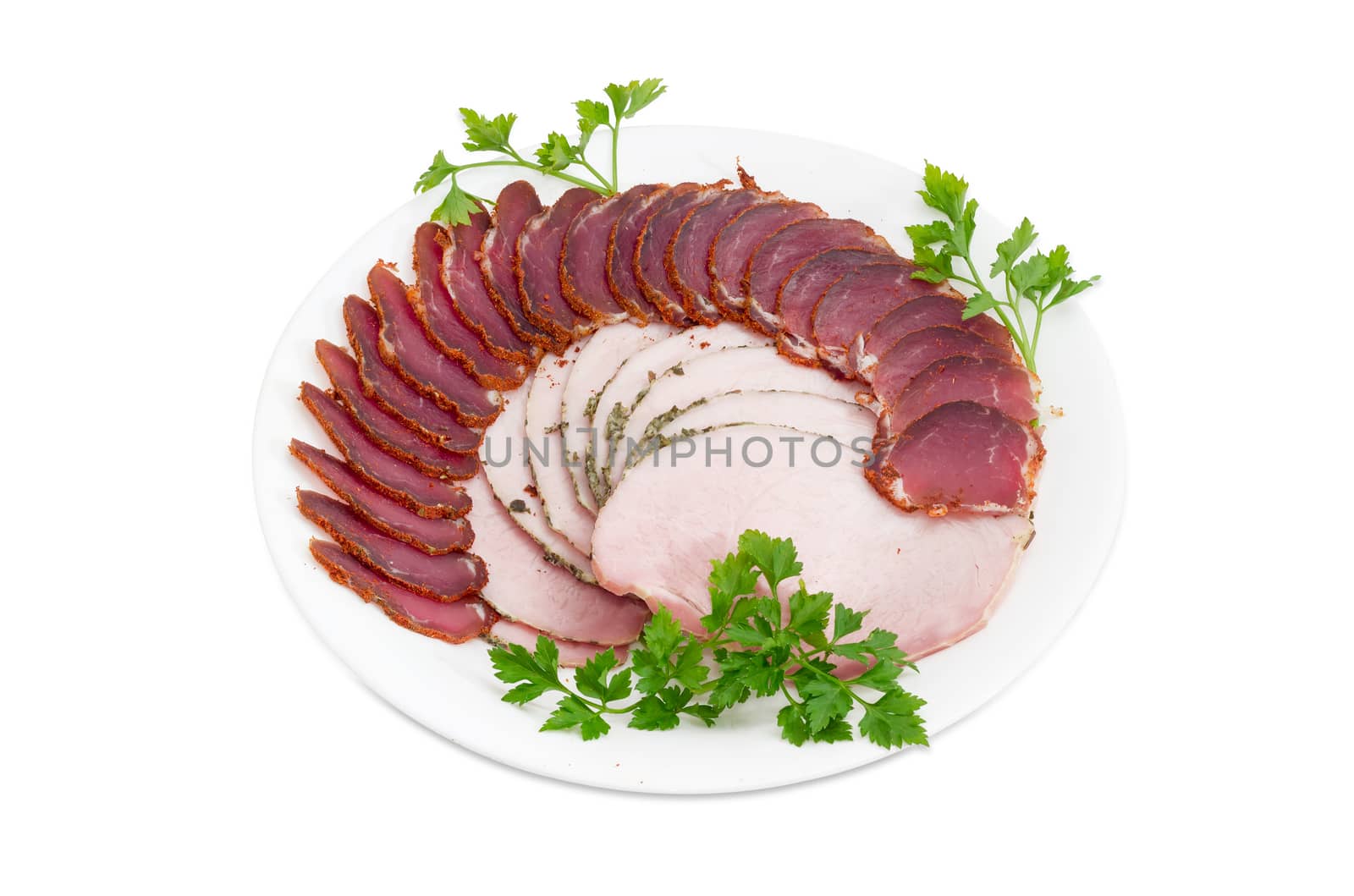 Sliced dried pork tenderloin and ham with twigs of parsley on a white dish on a light background 
