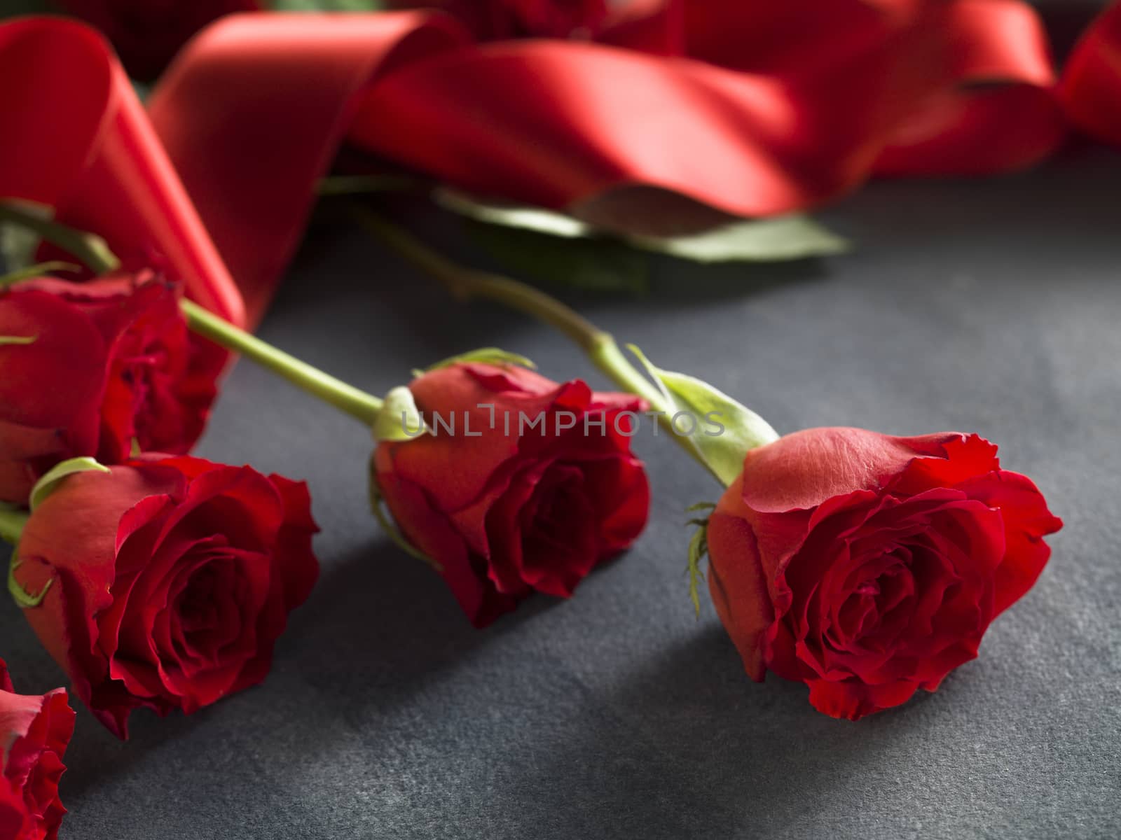 Close up red ribbon and red roses bouquet on a grey background