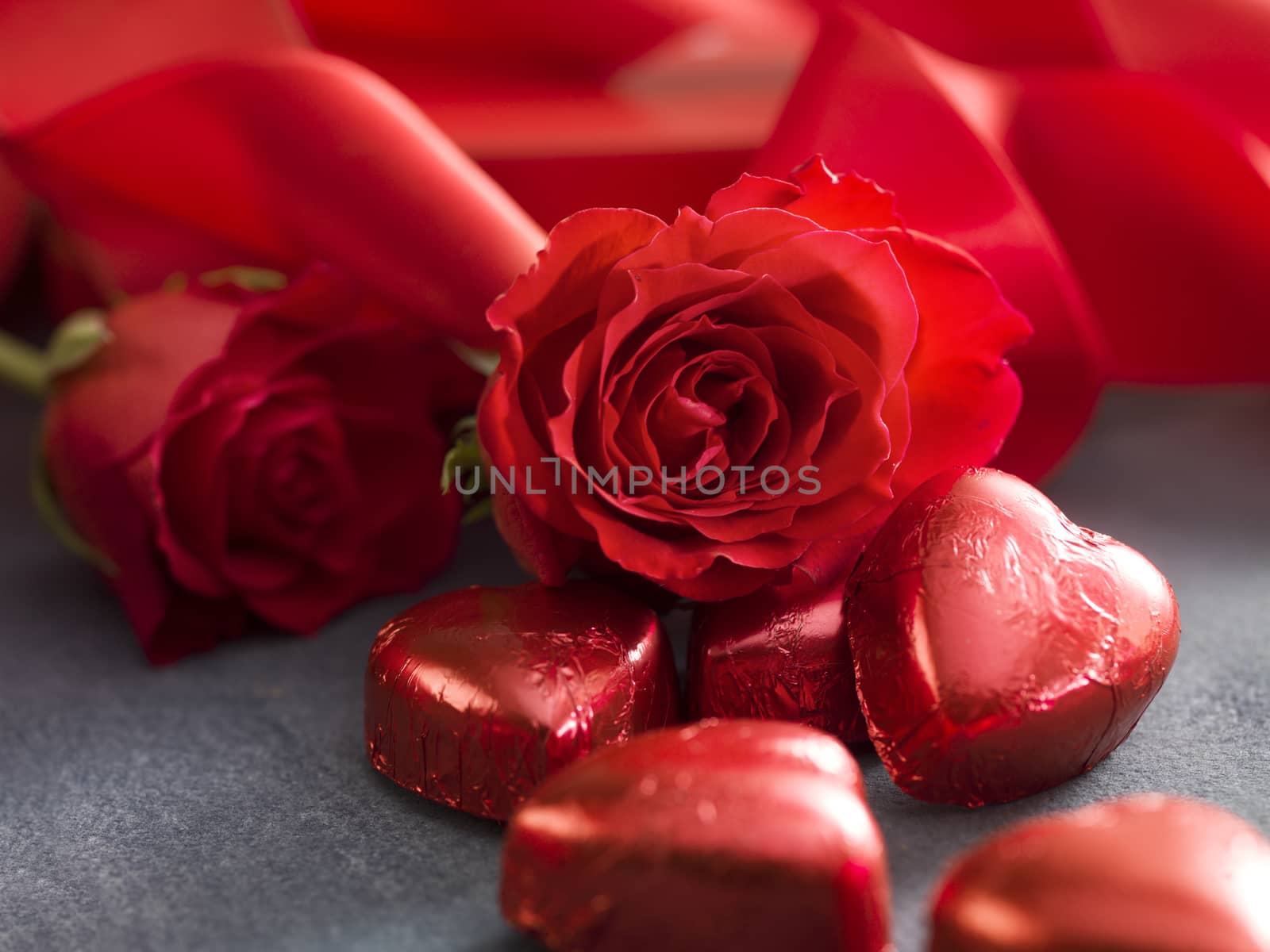 Hart shaped chocolate with valentine's day roses and red ribbon on grey background