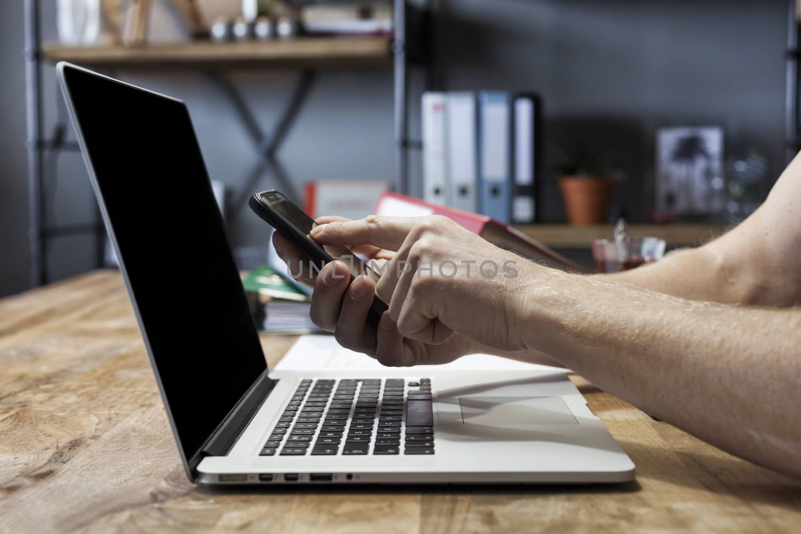 Man's hands holding a mobile phone and using laptop for online shopping