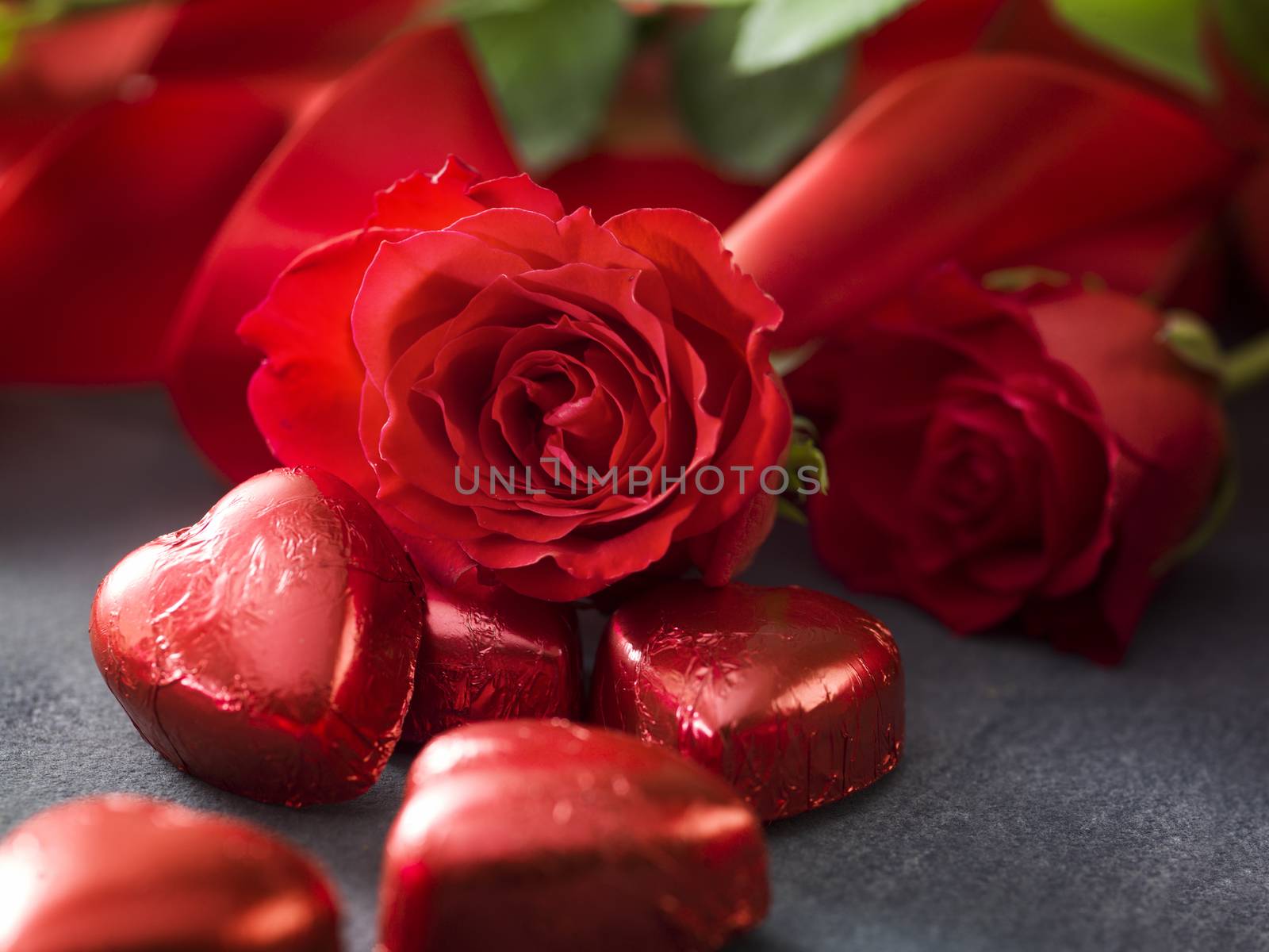 Valentine's day roses with red ribbon and hart shaped chocolate on grey background