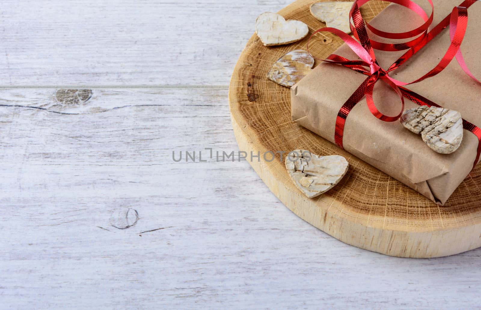 Box with a present to the Valentine's Day and wooden hearts lie on the white table