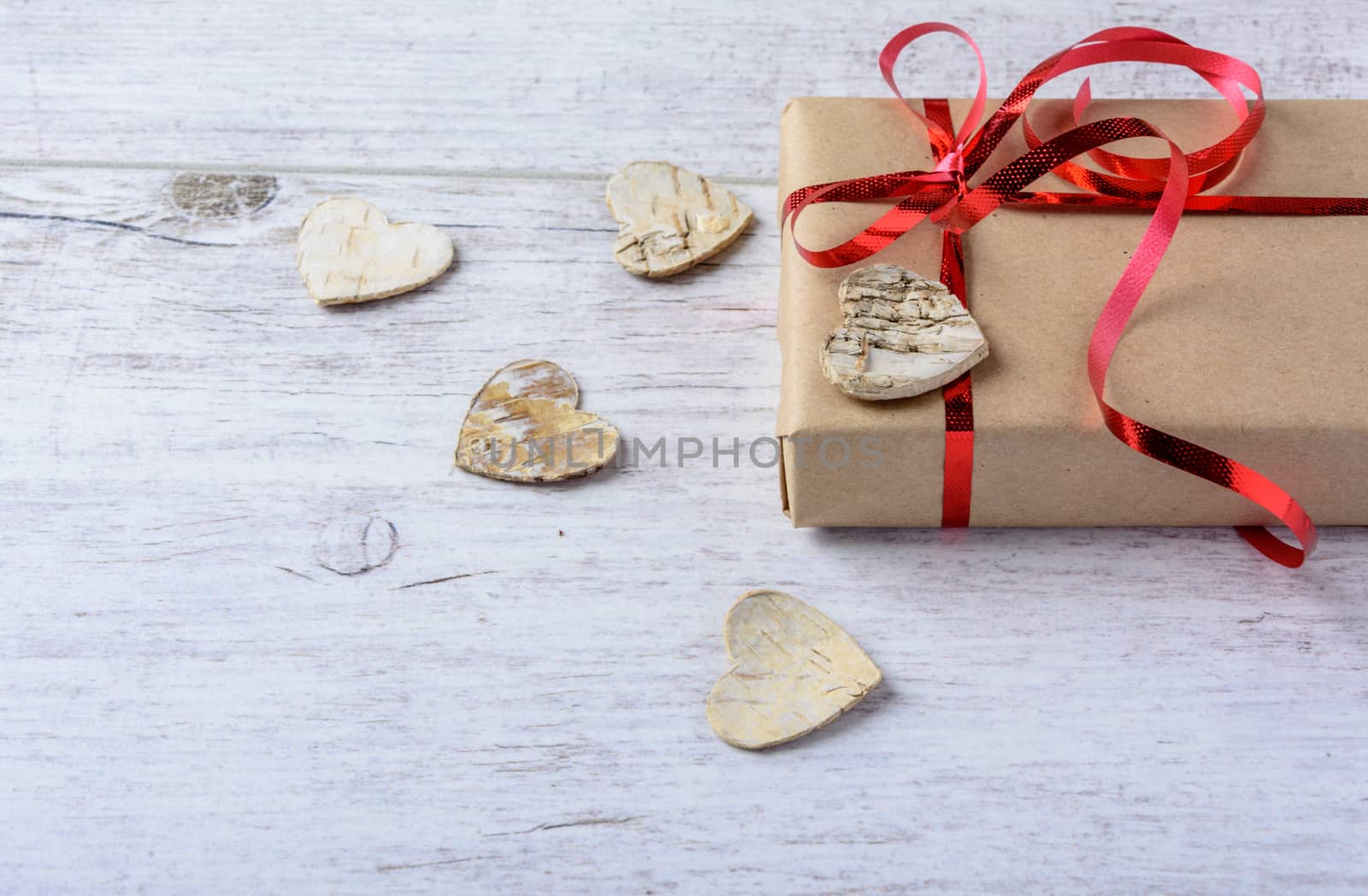 Box with a present to the Valentine's Day and wooden hearts lie on the white table