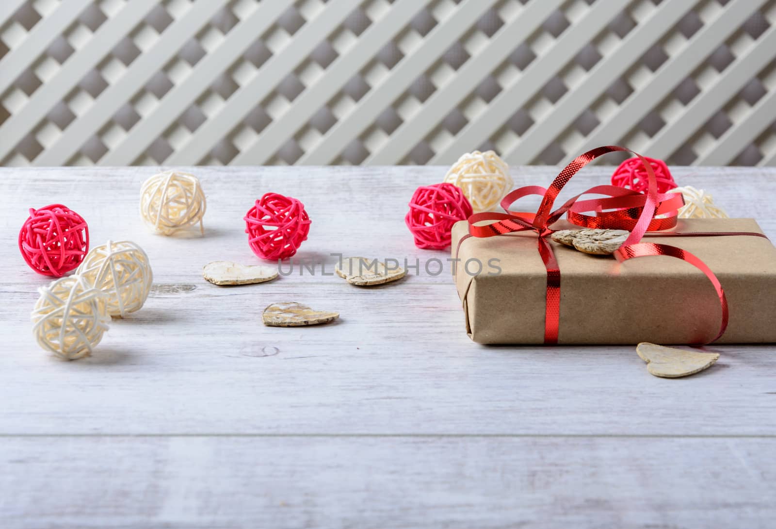 Box with a present to the Valentine's Day and wooden hearts and balls lie on the white table