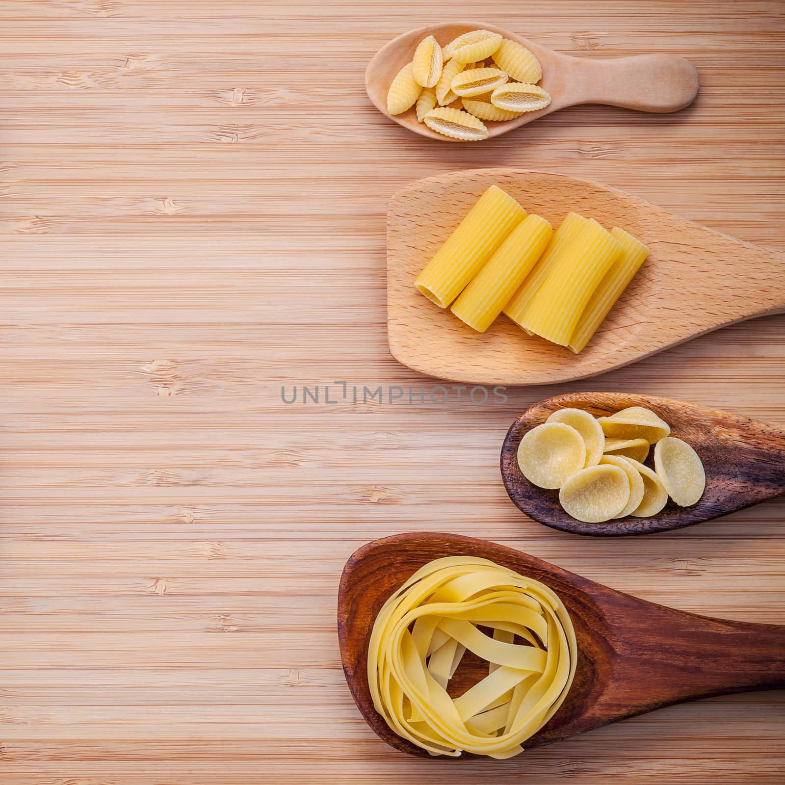 Italian foods concept and menu design . Various kind of Pasta Fettuccine ,Rigatoni ,Gnocco Sardo and orecchiette pugliesi in wooden spoons setup on bamboo cutting board flat lay and copy space.