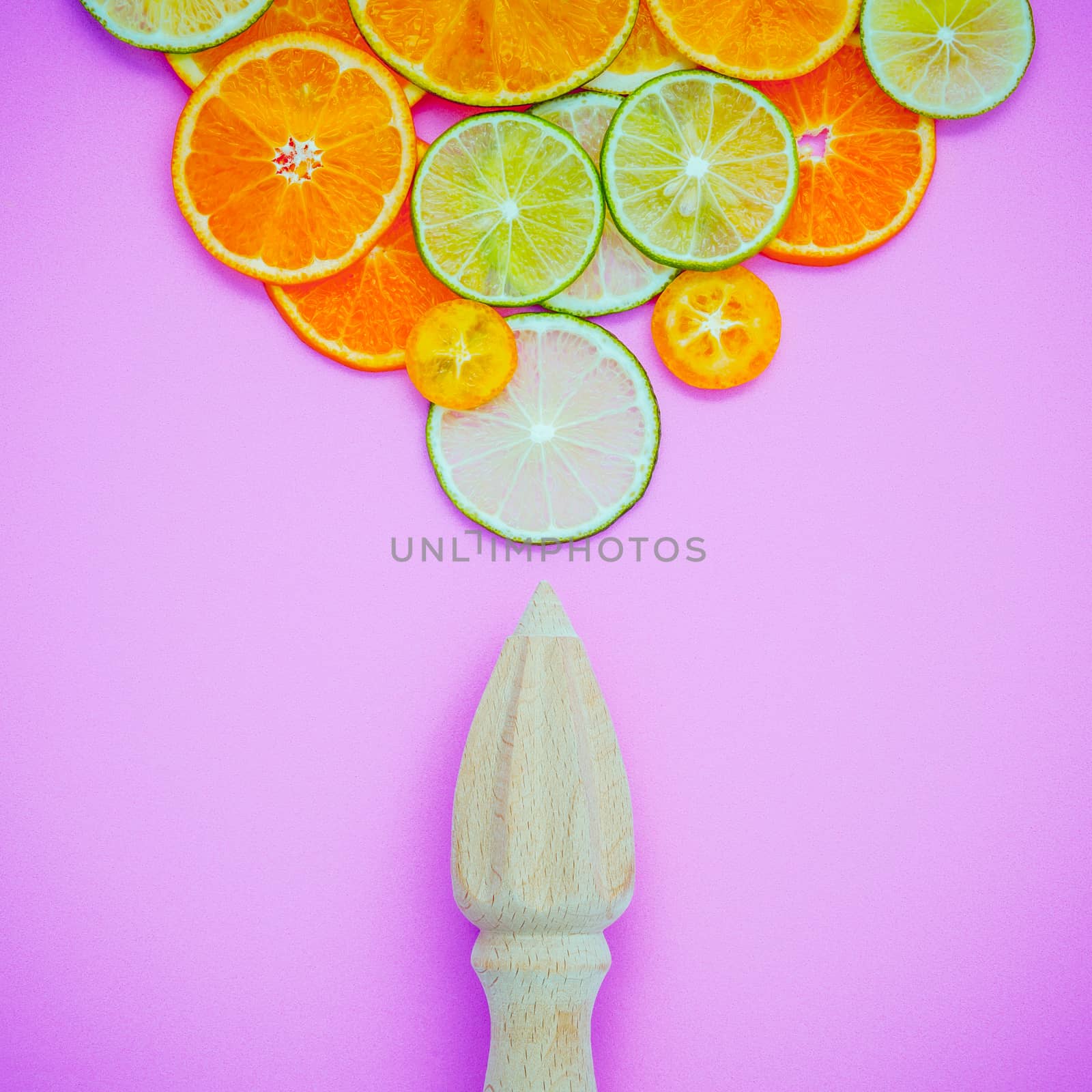 Mixed fresh citrus fruits and wooden juicer for summer citrus juice. Citrus fruits sliced lime,orange and lemon on light pink background flat lay.