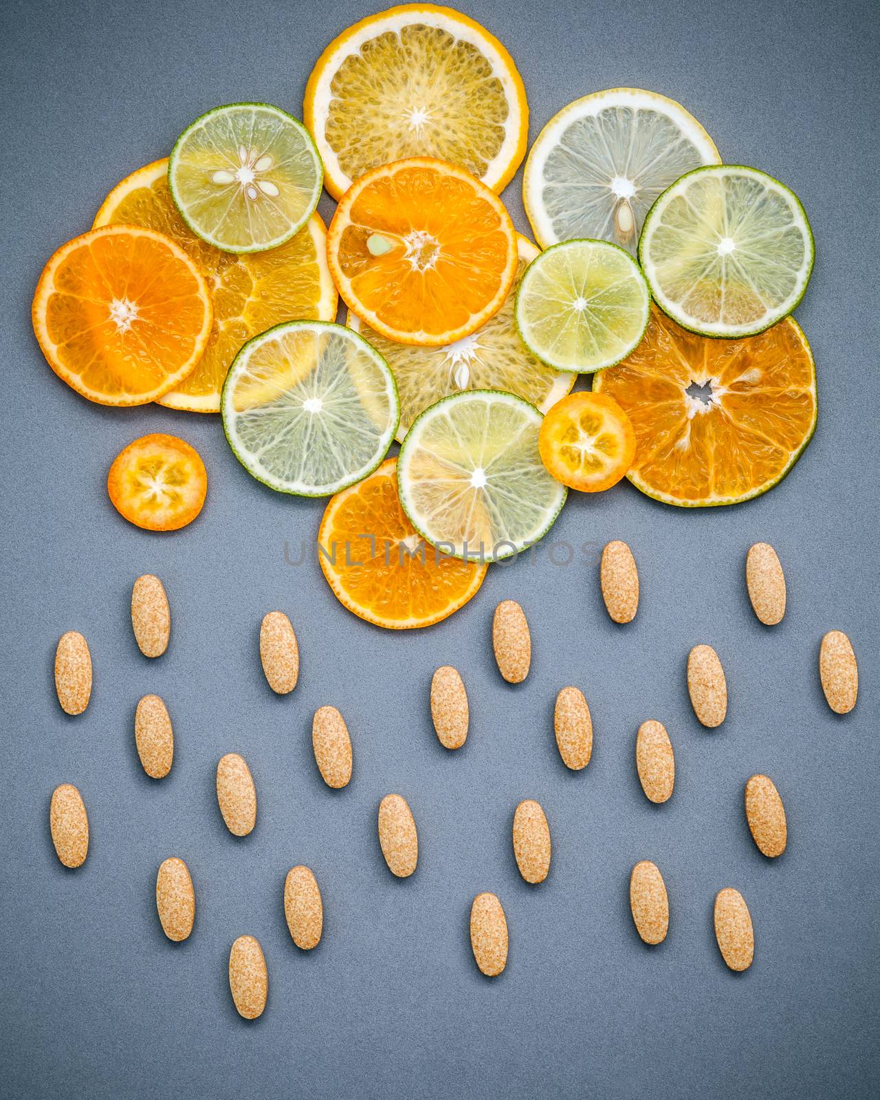 Healthy foods and medicine concept. Pills of vitamin C and various citrus fruits sliced in the shape of cloud and raining. Mixed citrus fruits sliced lime,orange ,kumquat and lemon on gray background.