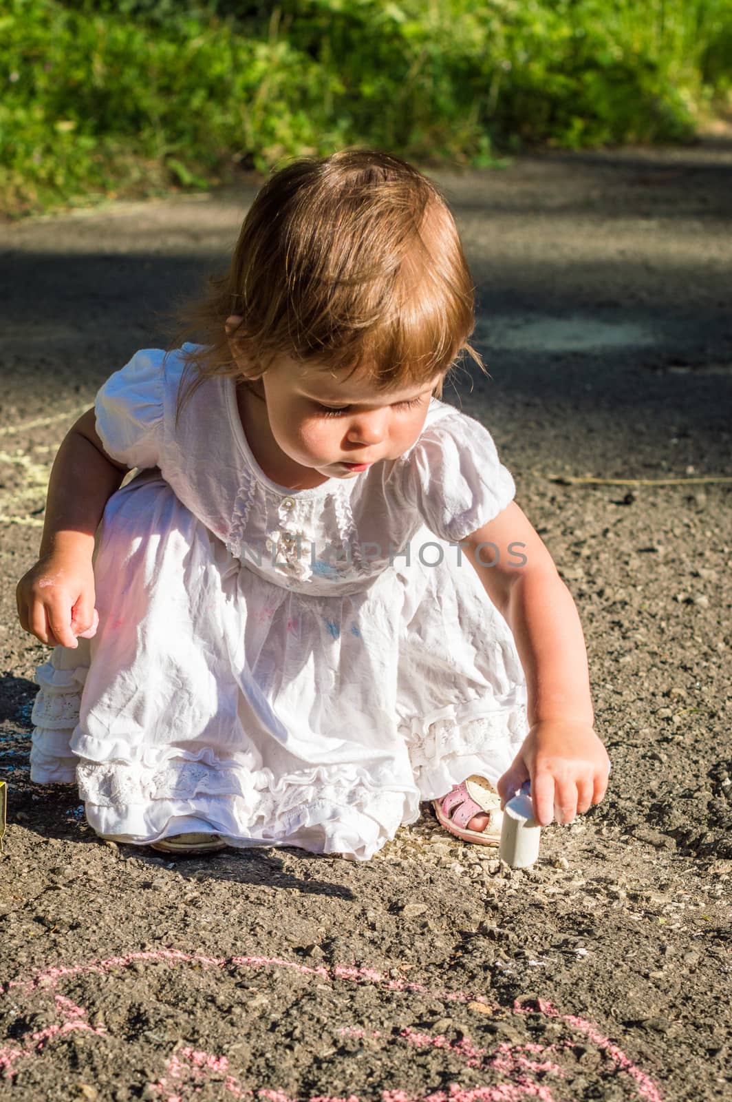 a little girl draws on asphalt in the Park in summer