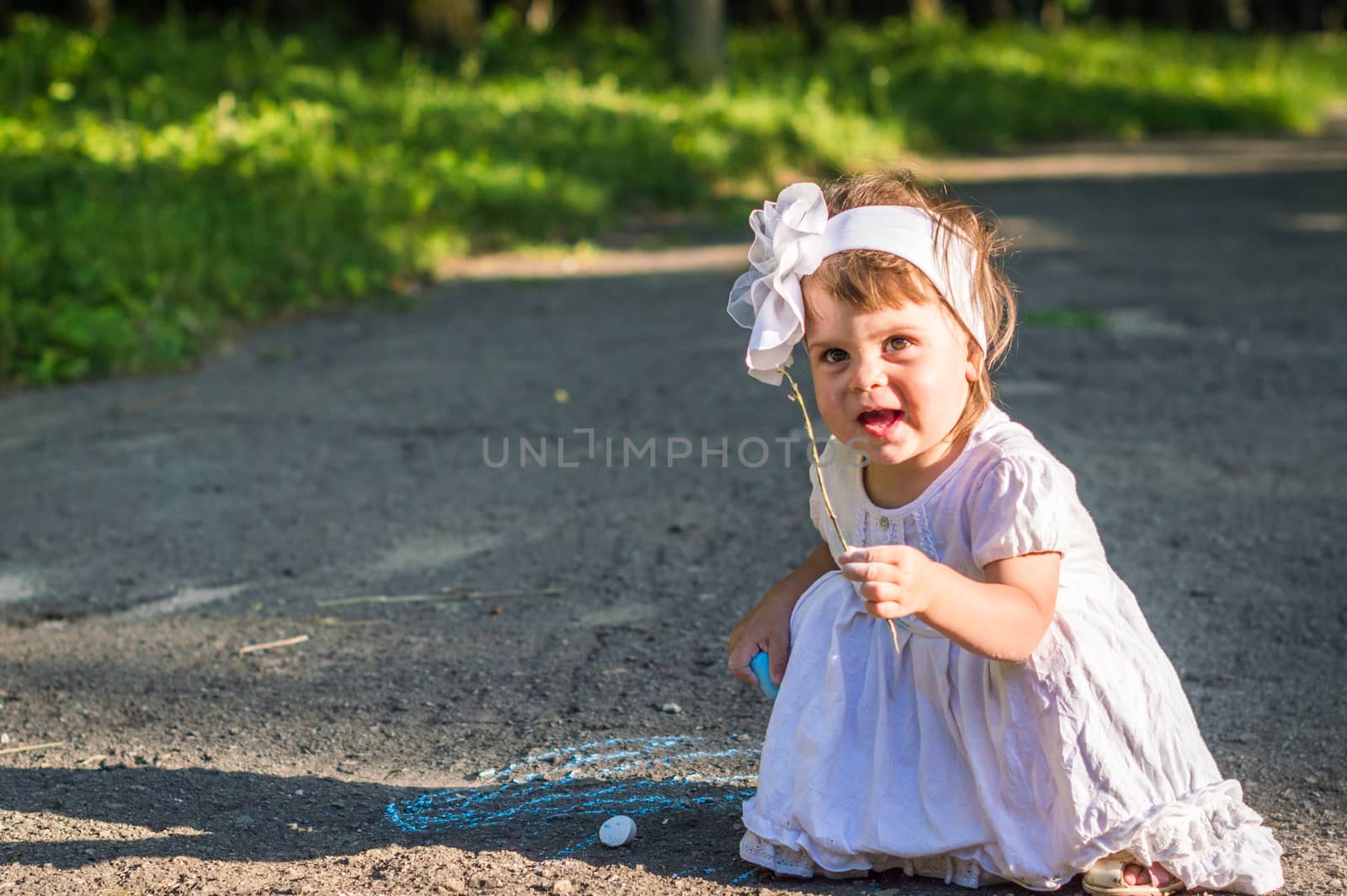 a little girl draws on asphalt in the Park in summer