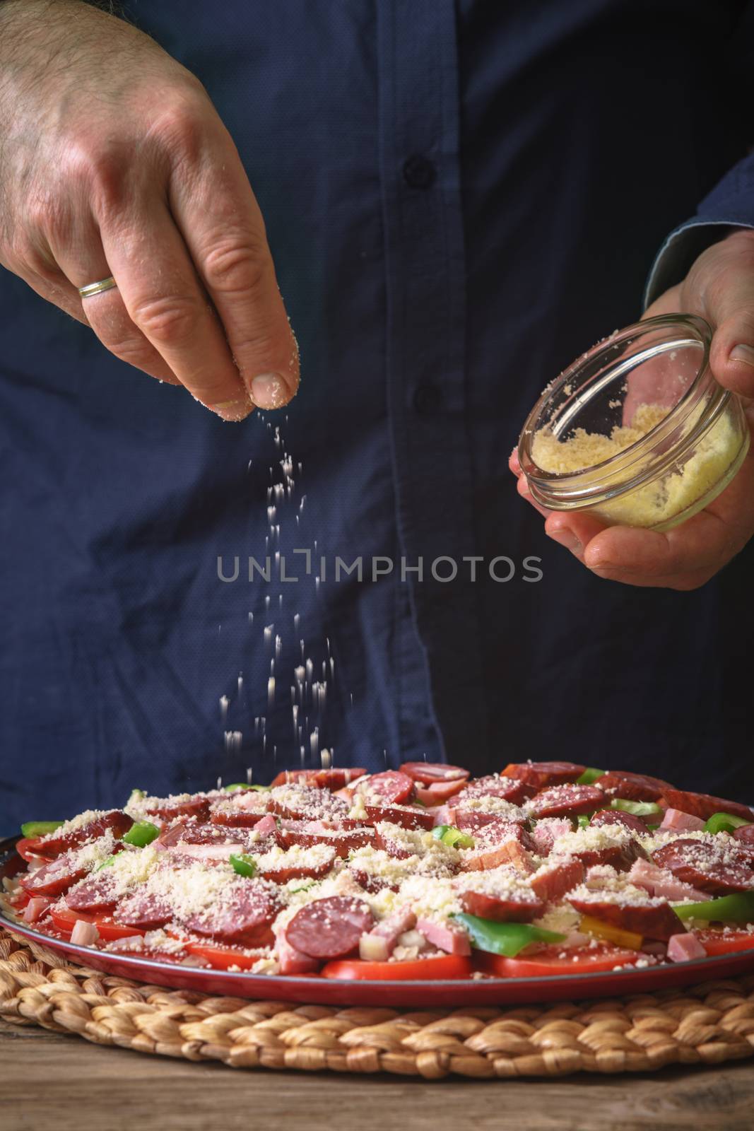 Man in a blue shirt sprinkle with cheese pizza from a sauser vertical