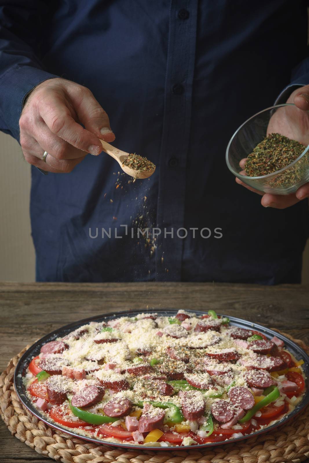 Man in a blue shirt sprinkle with spice pizza from a glass sauser vertical