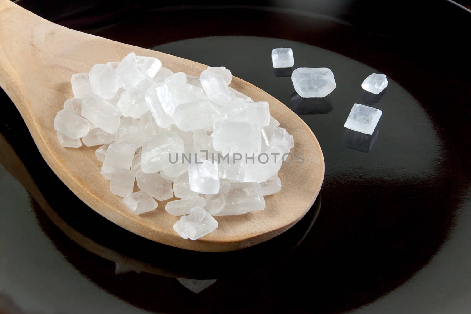 rock sugar white in a wooden spoon on the black background. Pure cane sugar for natural. no additives.