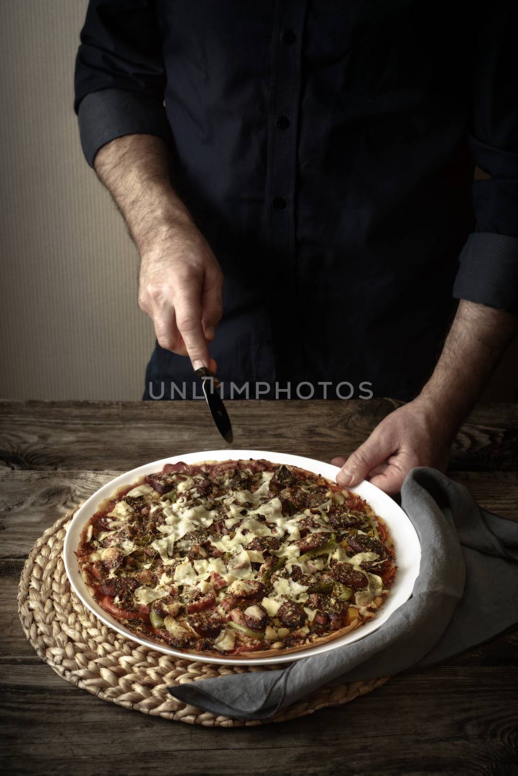 Man cuts the finished pizza on a white dish vertical