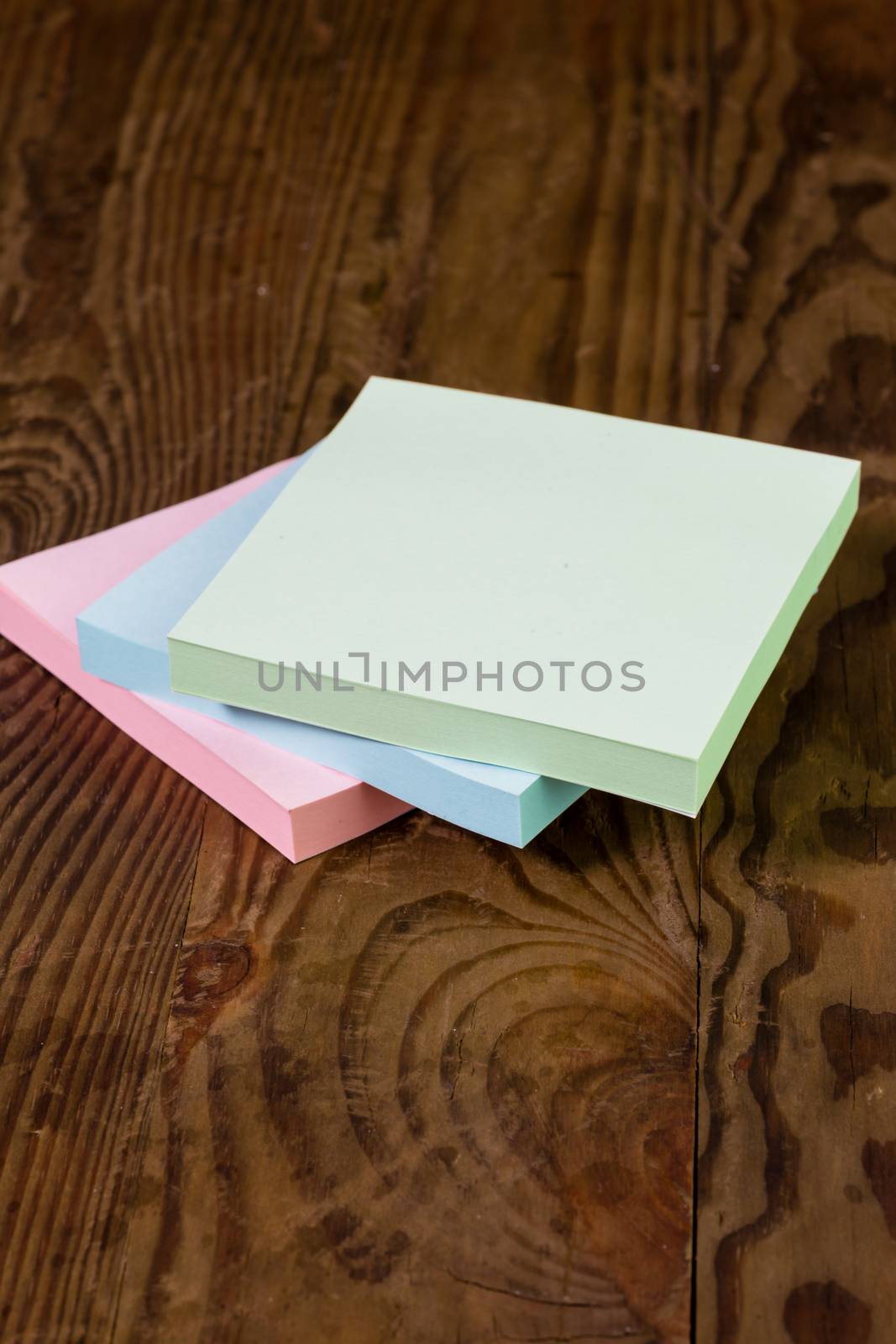 Stack of different colored notepads on ditressed wood background, shallow DOF