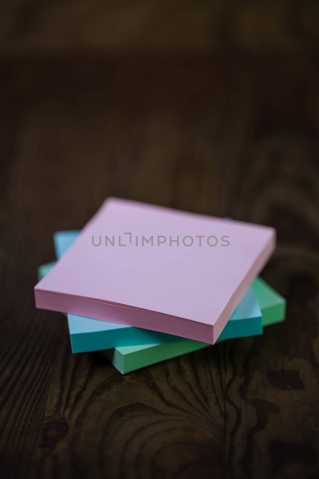 Stack of different colored notepads on ditressed wood background, shallow DOF